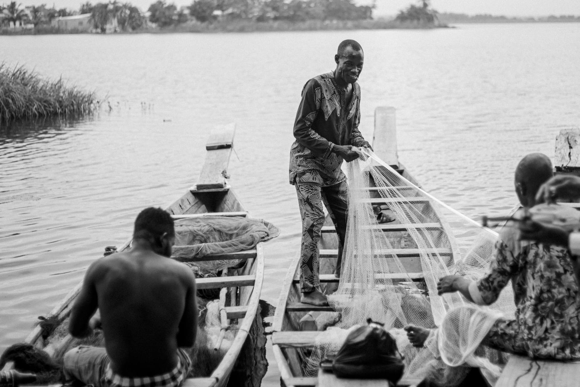 Dugout canoes resting on the rust-red shore of Lake Volta at dawn, with mist sitting low over the still water near Akosombo