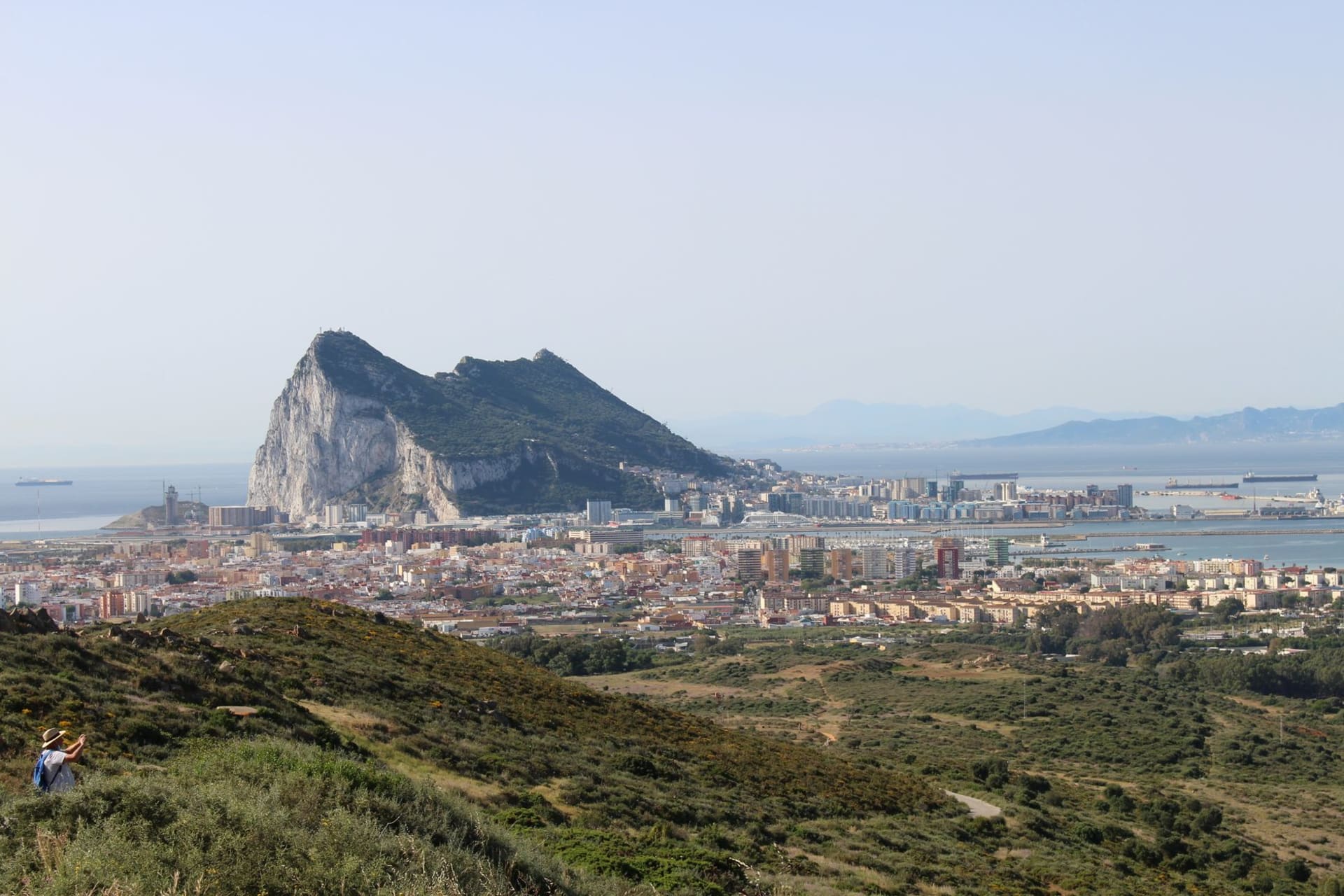The Tower of Homage of the Moorish Castle rising above Gibraltar's rooftops with the Rock face behind it under a deep blue sky