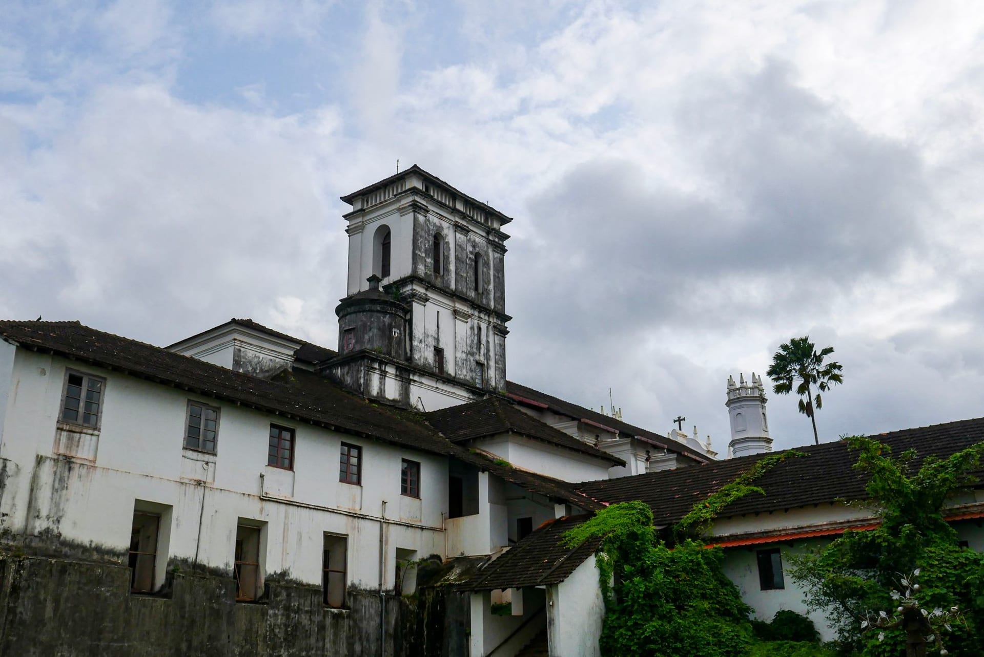 A whitewashed Portuguese colonial church with twin bell towers rising above lush green grounds in Goa, India