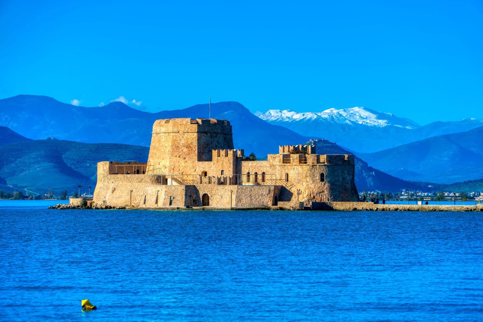 The Palamidi fortress rising on a rocky cliff above Nafplio's terracotta rooftops, with the calm Argolic Gulf shimmering in the afternoon light below