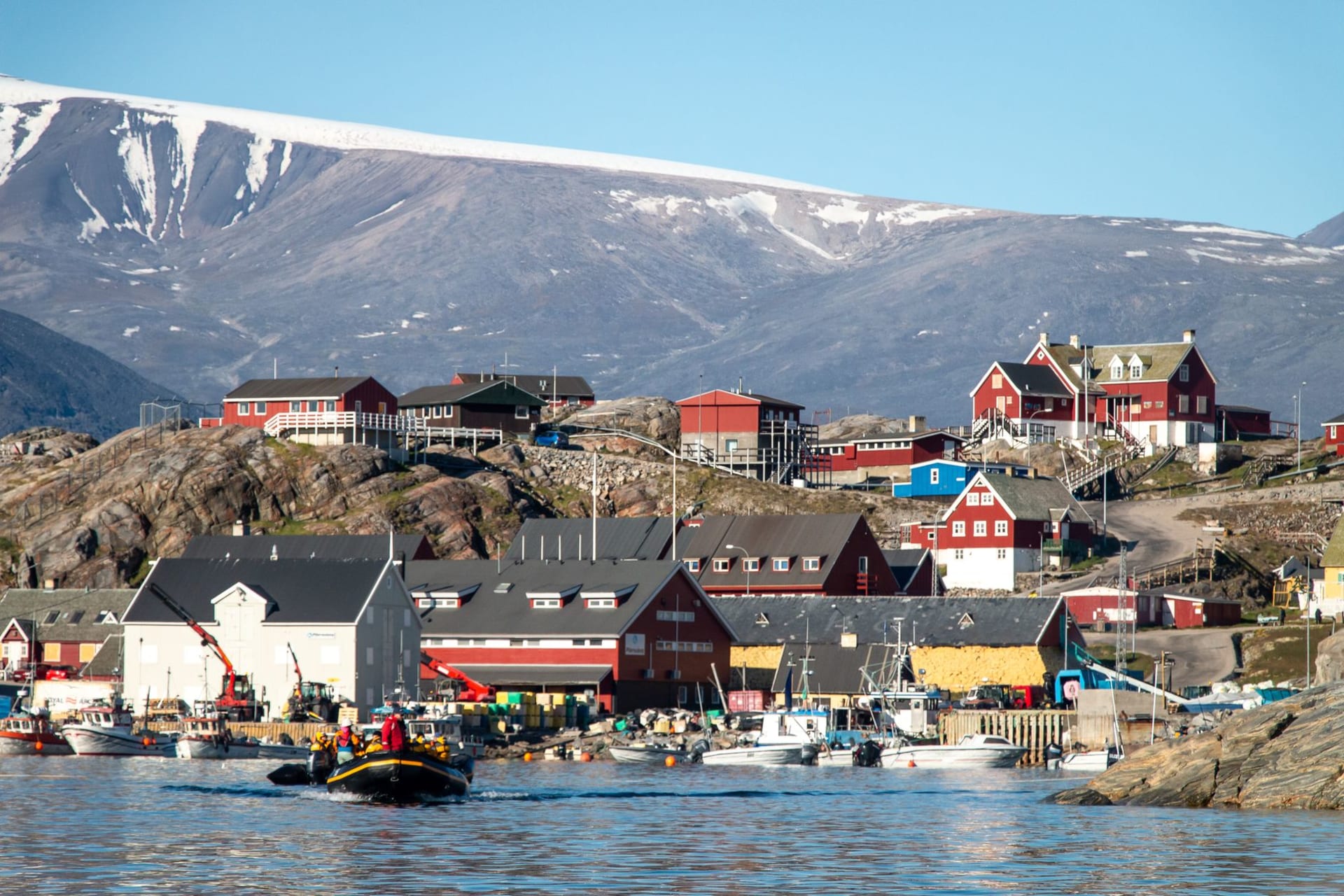 Uummannaq island town with red and yellow houses beneath the dramatic heart-shaped mountain peak, surrounded by sea ice and floating icebergs