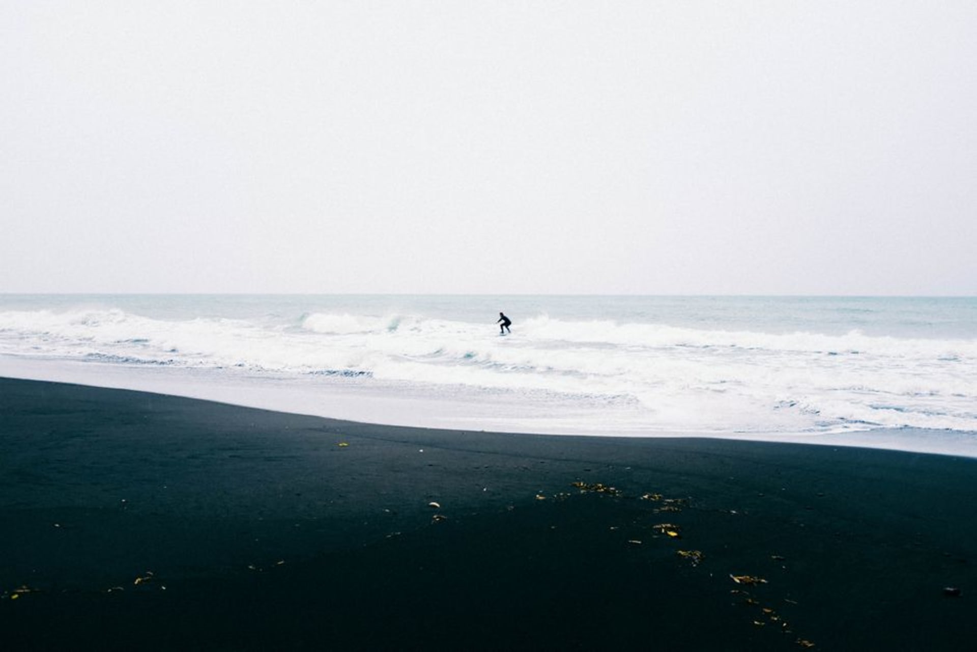 Una playa de arena volcánica negra en El Paredón, Guatemala, con surfistas remando hacia las olas del Pacífico al atardecer