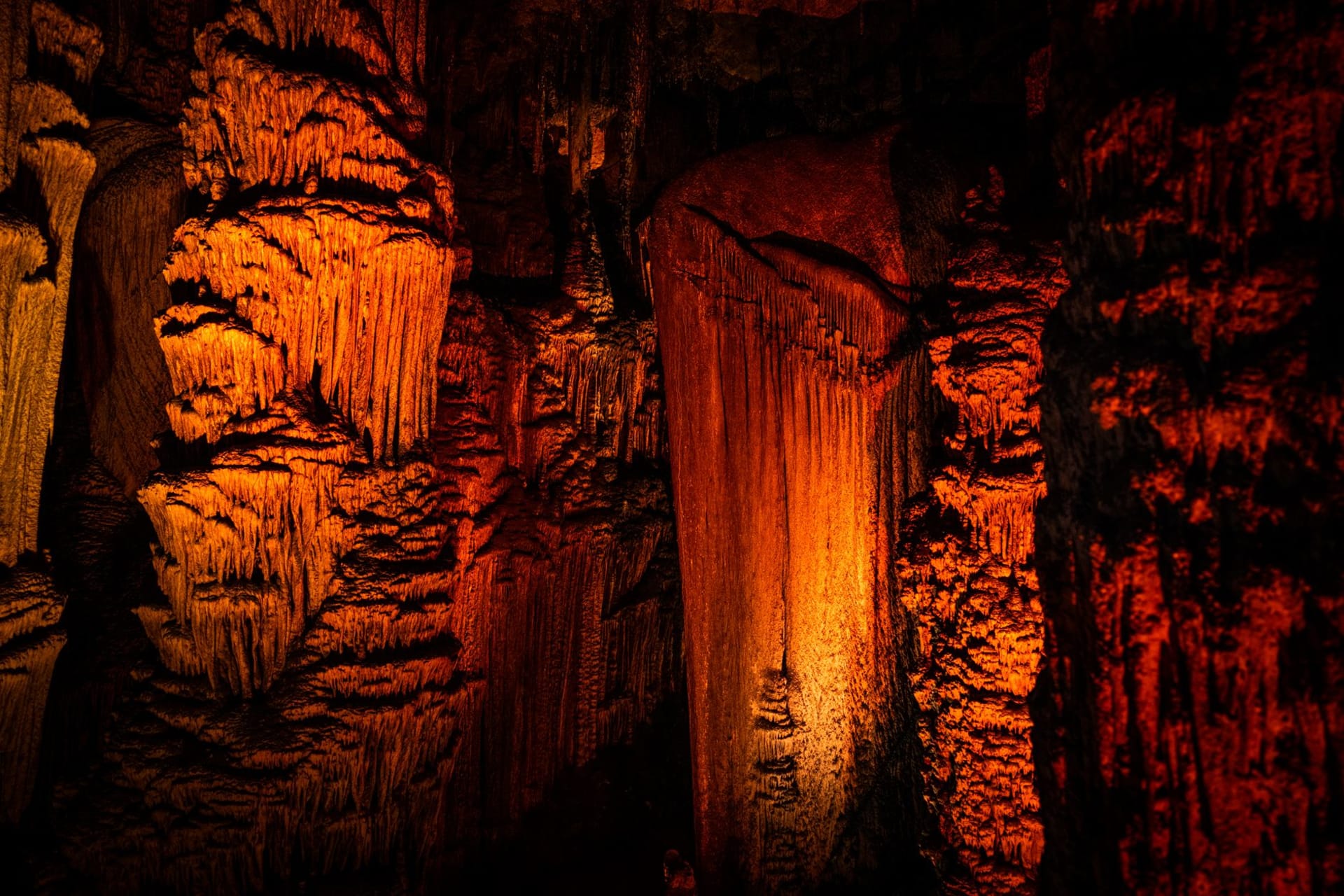Vaste chambre à l'intérieur de la Grotte de la Flûte de Roseau éclairée en violet et or, stalactites suspendues au plafond au-dessus d'un lac souterrain immobile