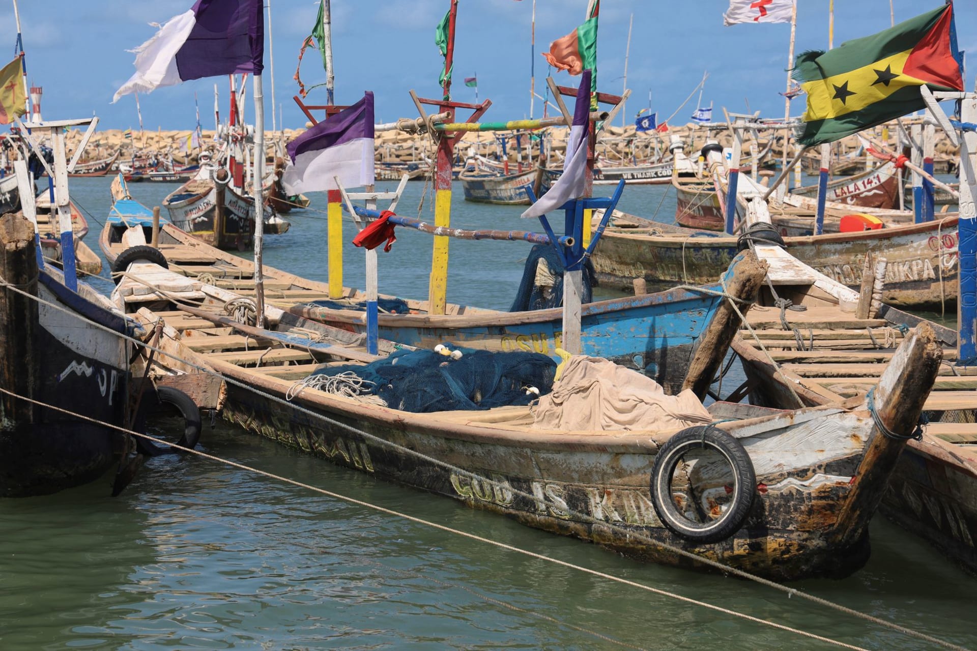 A narrow pirogue loaded with passengers crossing between islands, the water flat and silver at low tide, mangroves in the distance