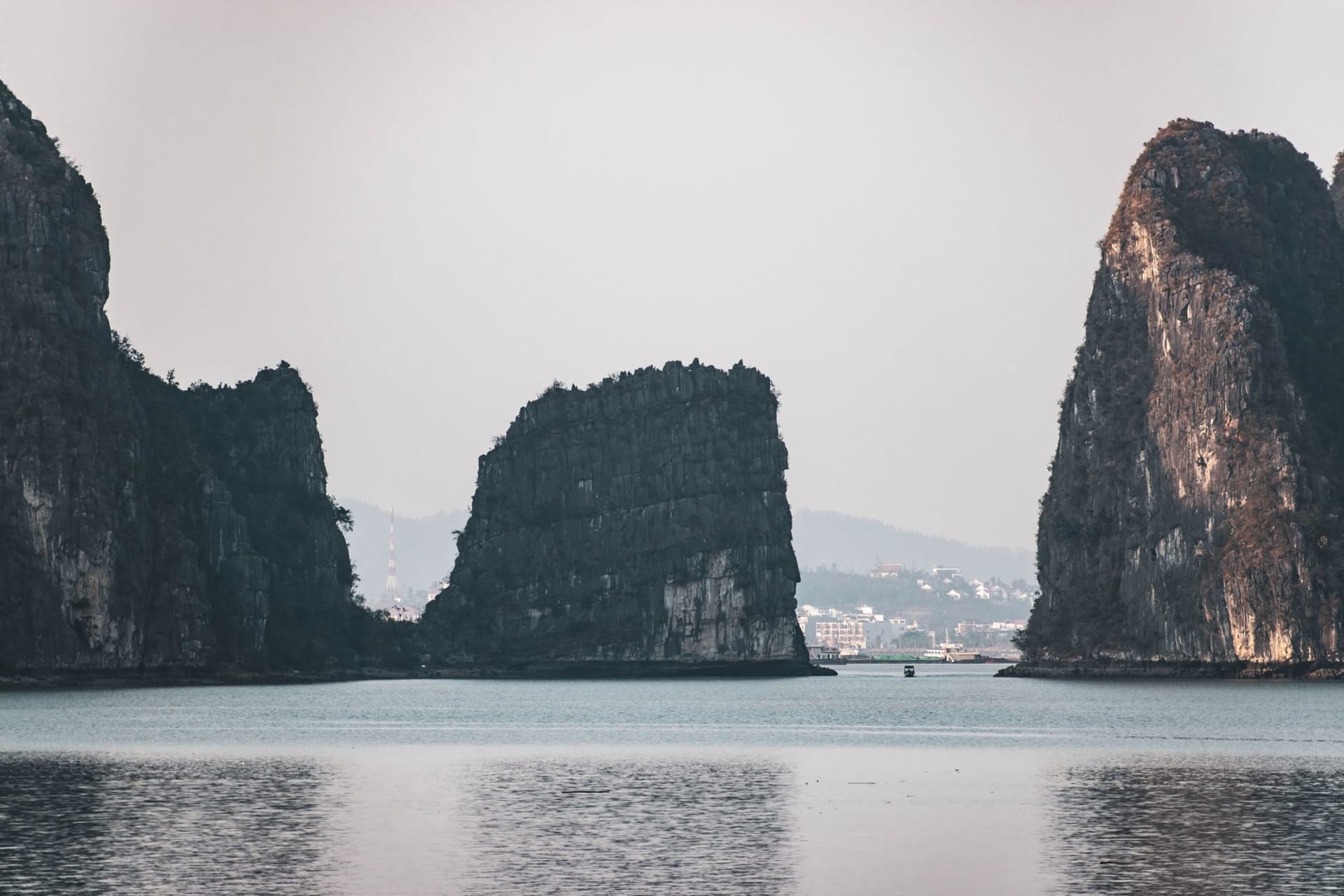 Cat Ba Town harbor at dusk with colorful fishing boats moored at the jetty and limestone karsts rising in the background