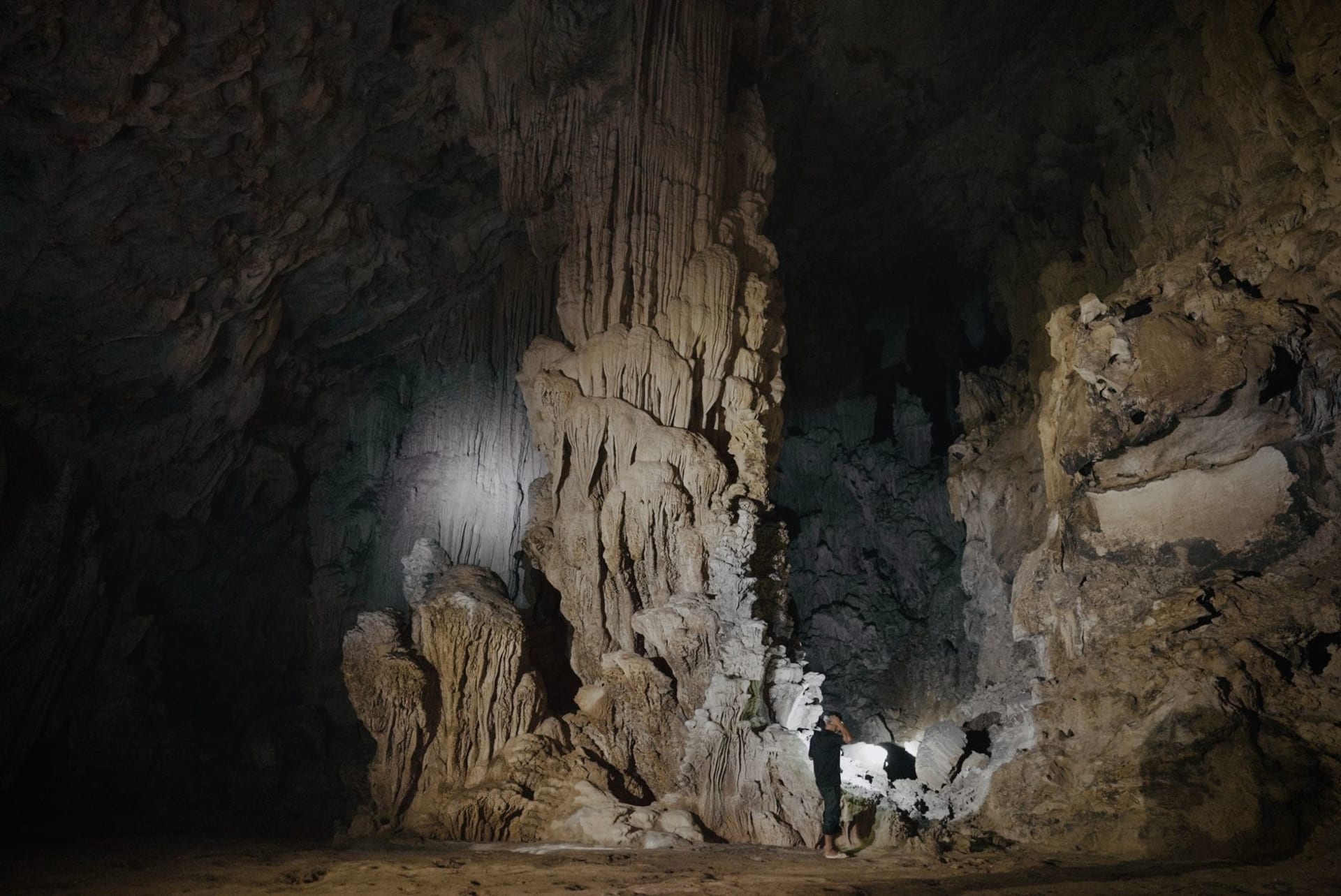 Interior of Dau Go Cave with towering stalactites and natural light entering through a high opening, illuminating ancient amber-colored limestone formations