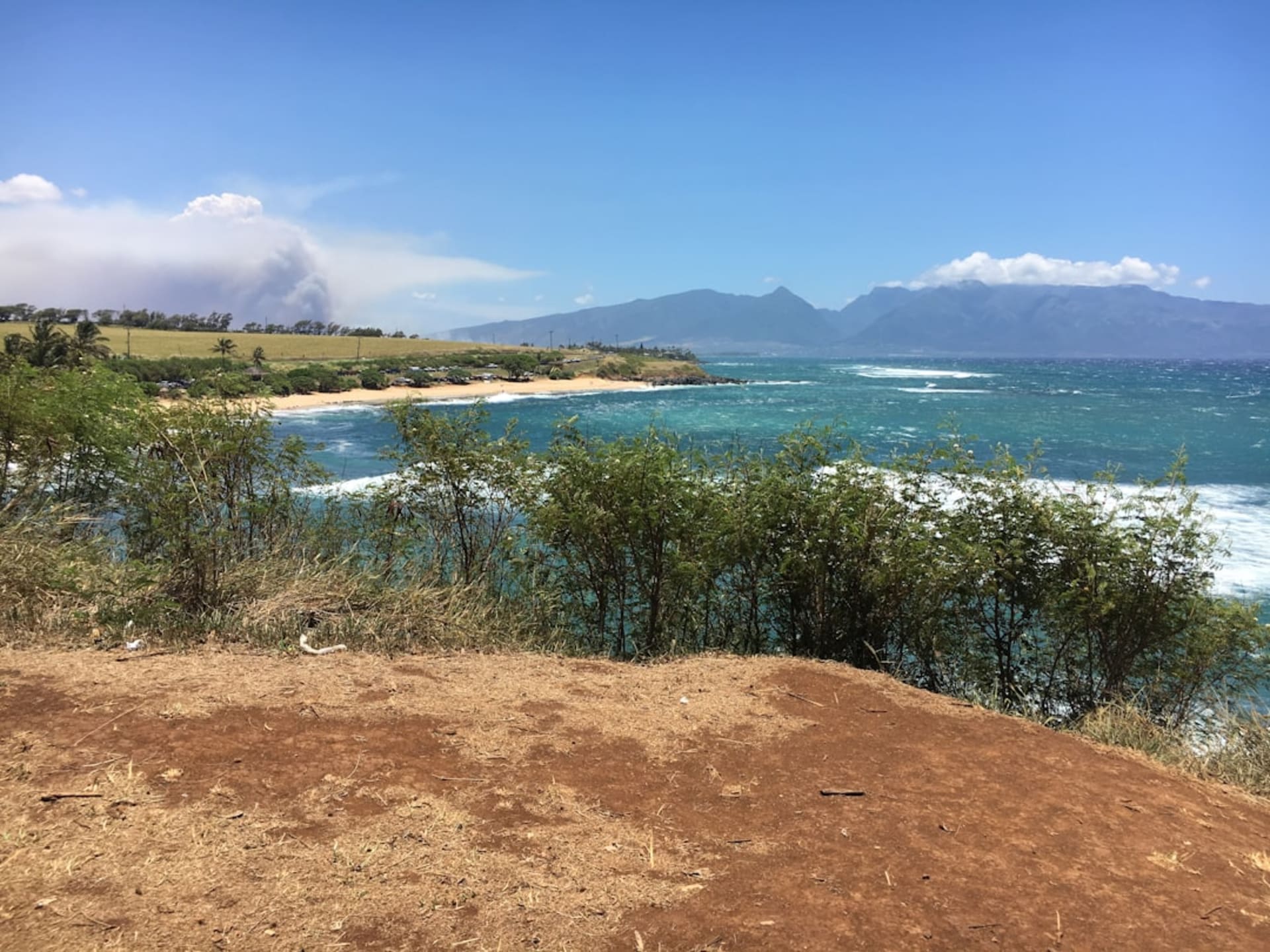 Wide sandy bay at Anahola Beach with green mountains rising behind the shoreline.