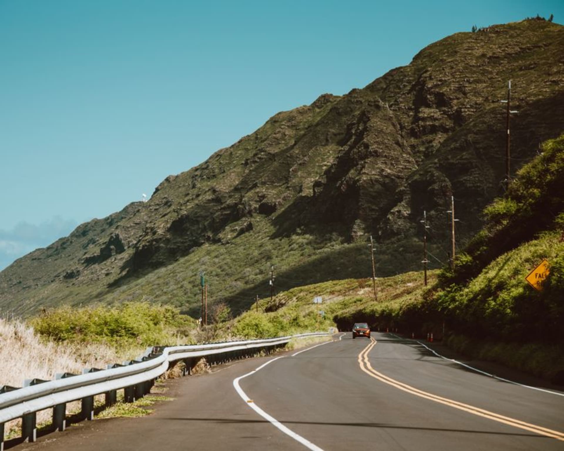 Narrow coastal road on Molokai's east end winding along cliffs above the ocean with dense green jungle