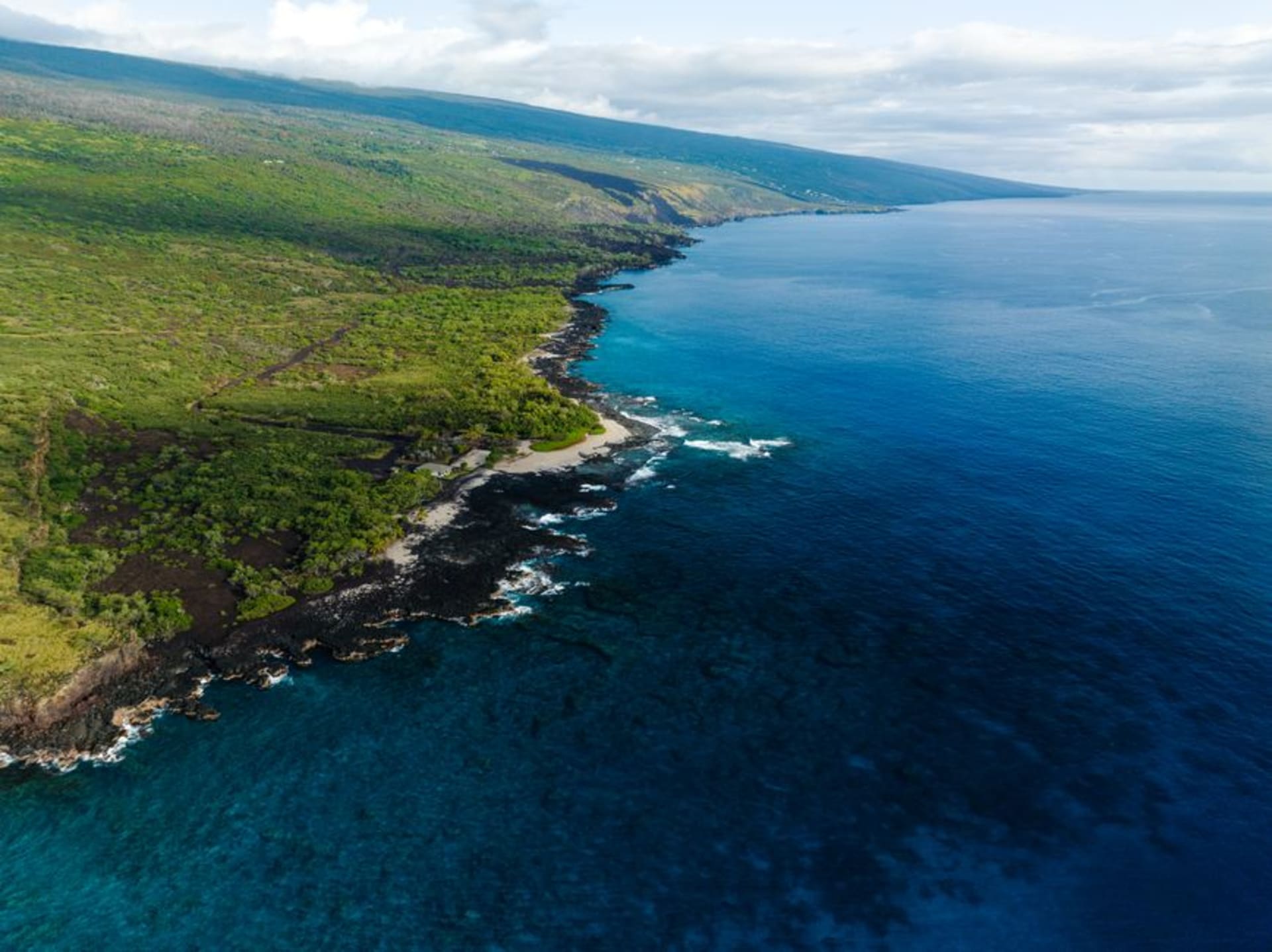 Kealakekua Bay's turquoise water with the white Captain Cook Monument visible against a black lava cliff