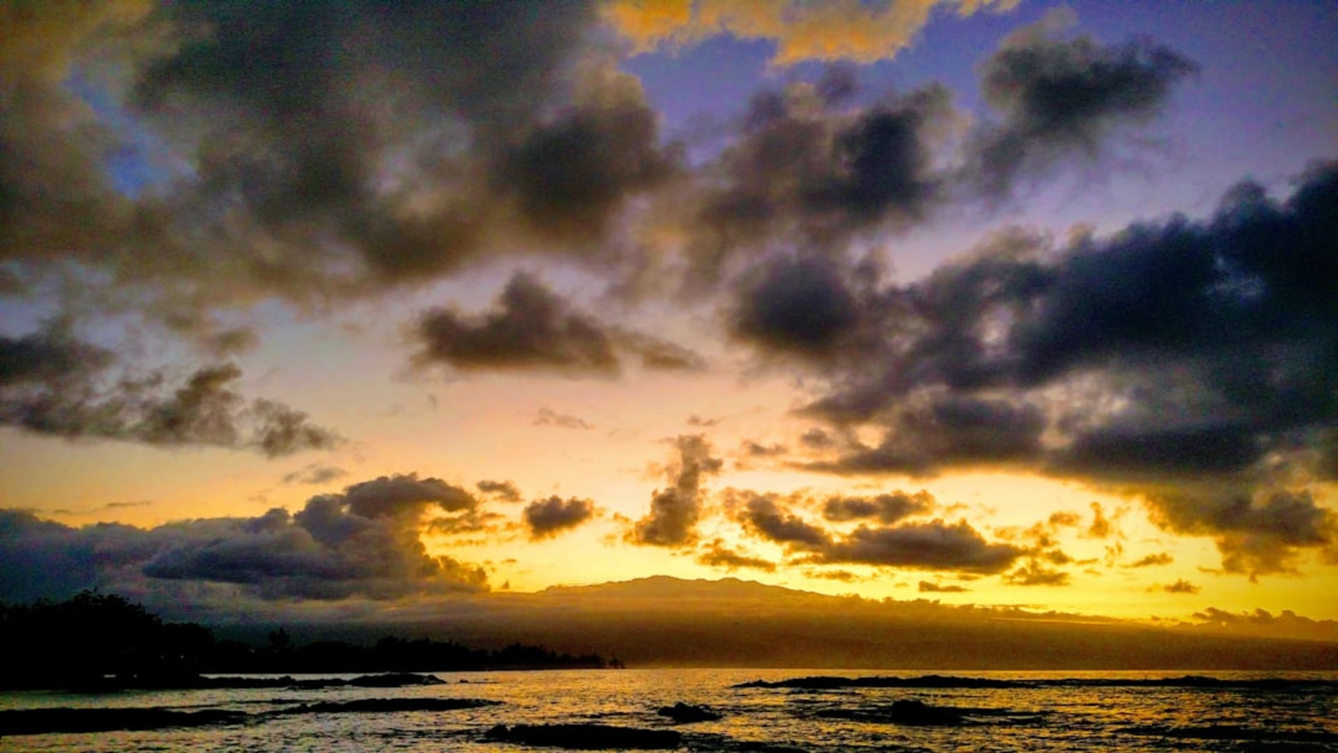 Mauna Kea summit at sunset with observatory domes silhouetted against a band of orange and purple sky