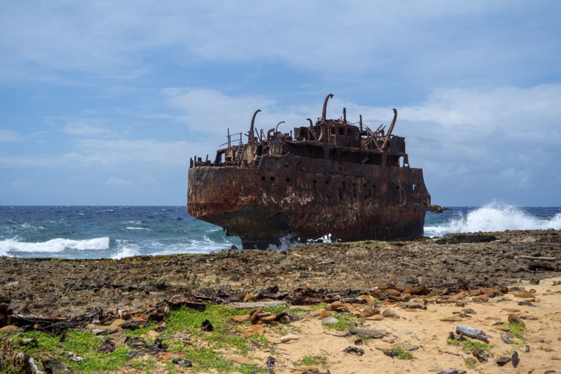 Coque rouillée d'une épave visible au large de Shipwreck Beach sur Lanai, avec un ressac agité et une côte battue par les vents