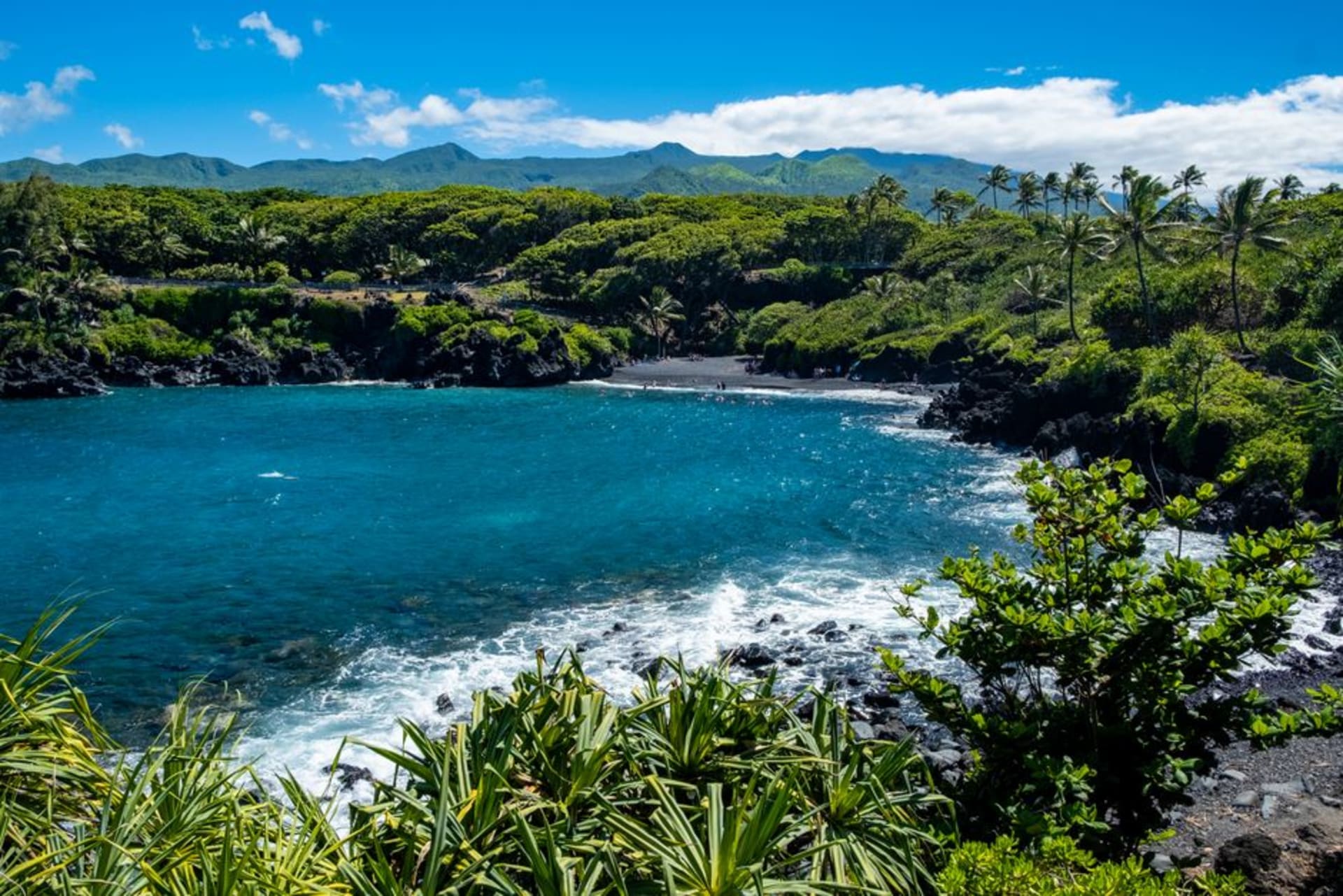 Black volcanic sand beach at Wai'anapanapa State Park with turquoise water and green cliffs on Maui's Hana Highway