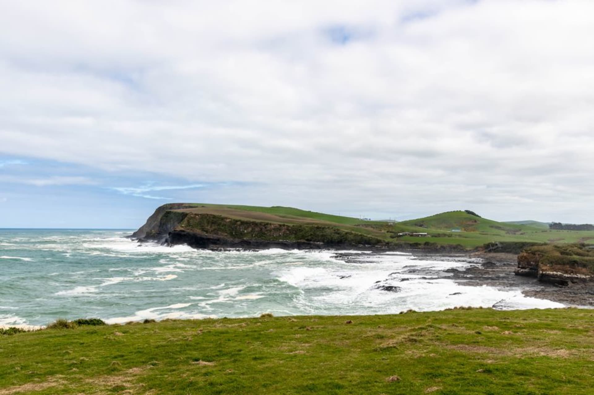 La pointe rocheuse nue et balayée par le vent du cap Erimo avec des vagues à crêtes blanches s'écrasant contre la roche noire et un phare au loin