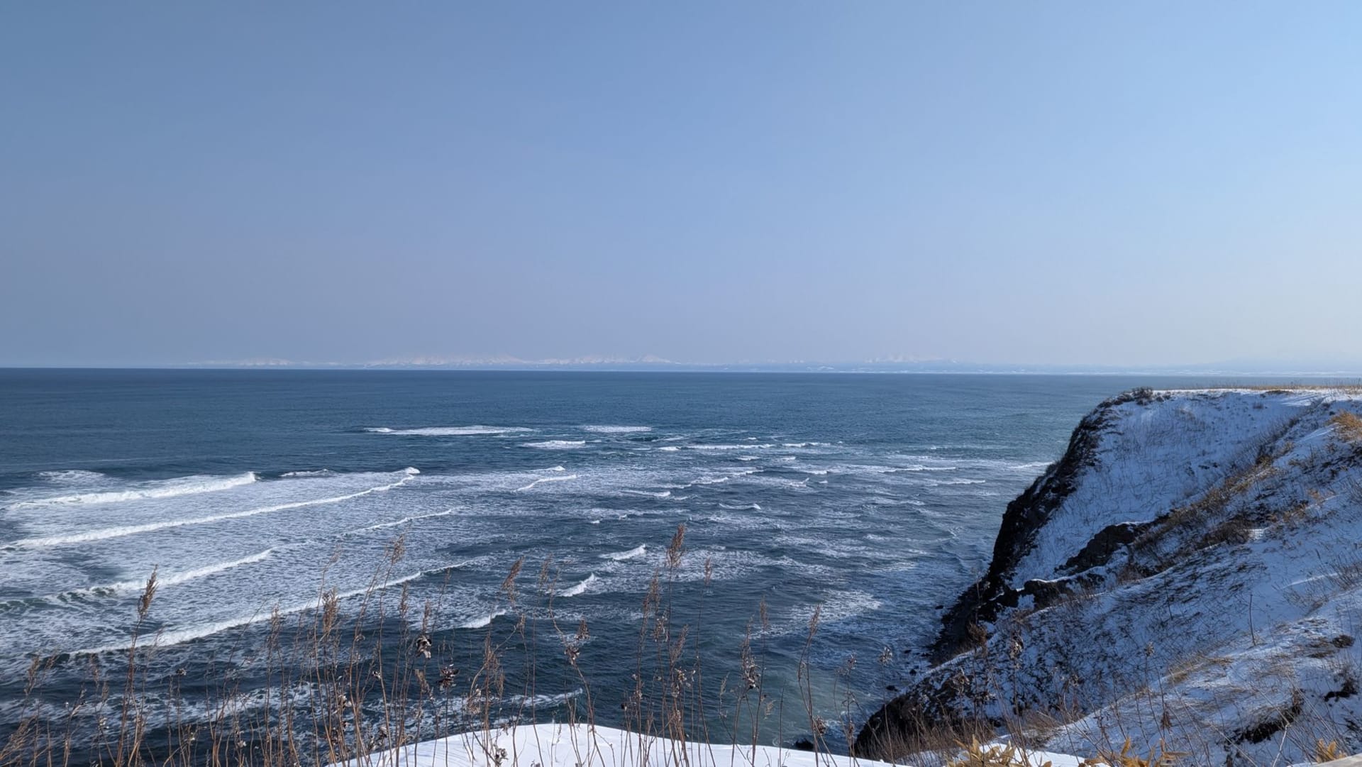 Snow-covered cliffs of Cape Shiretoko rising above deep blue ocean waves in winter