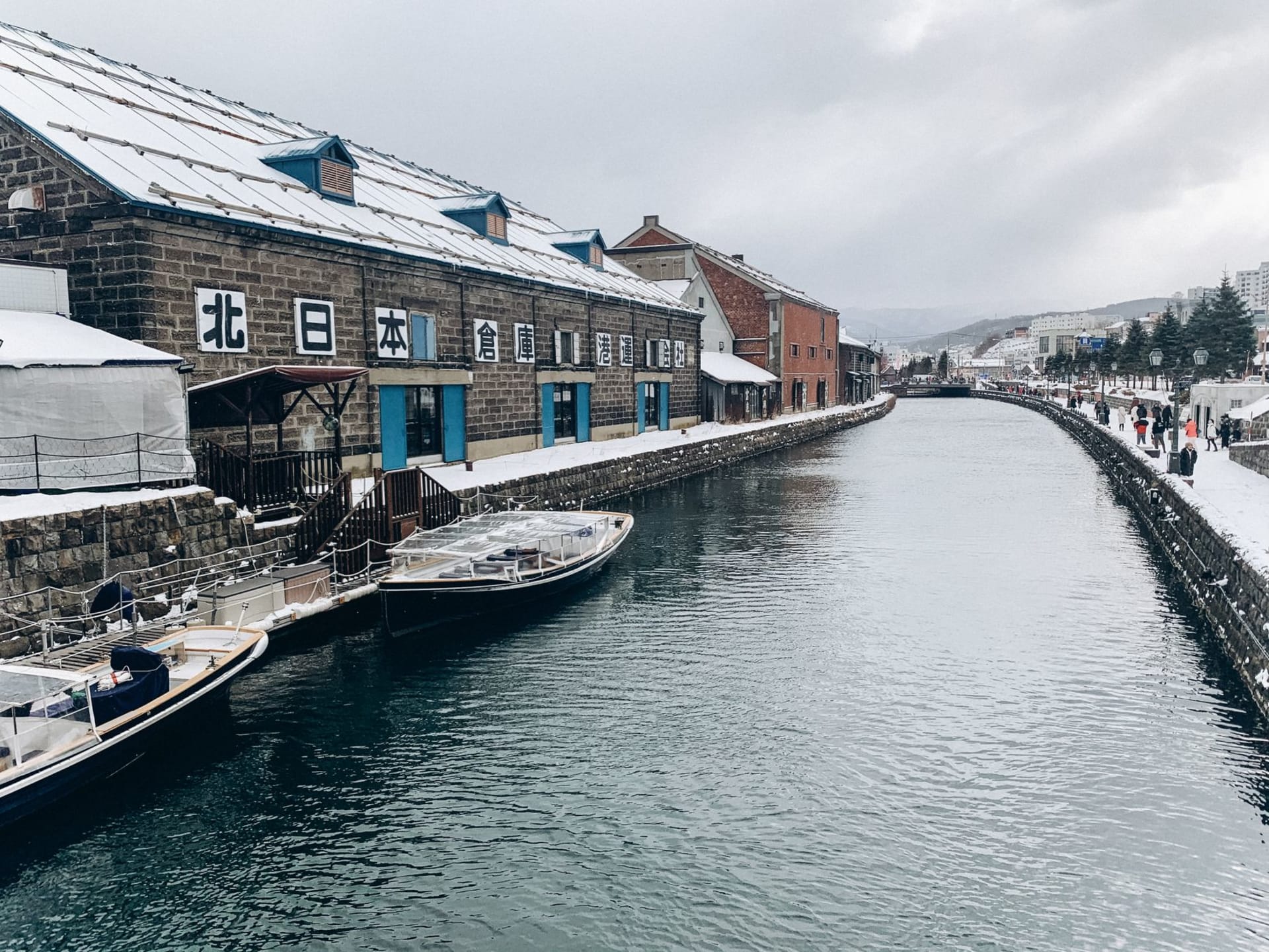 Otaru Canal at dusk, gas lanterns reflecting on the water between brick warehouses converted into restaurants and cafes, snow dusting the banks