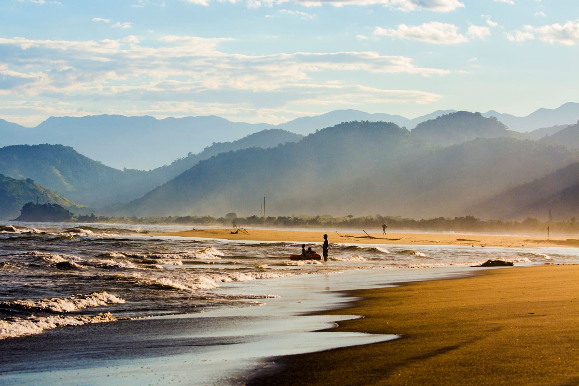 A long empty Caribbean beach at golden hour with palm trees leaning toward the water and a Garífuna fishing boat pulled up on the sand
