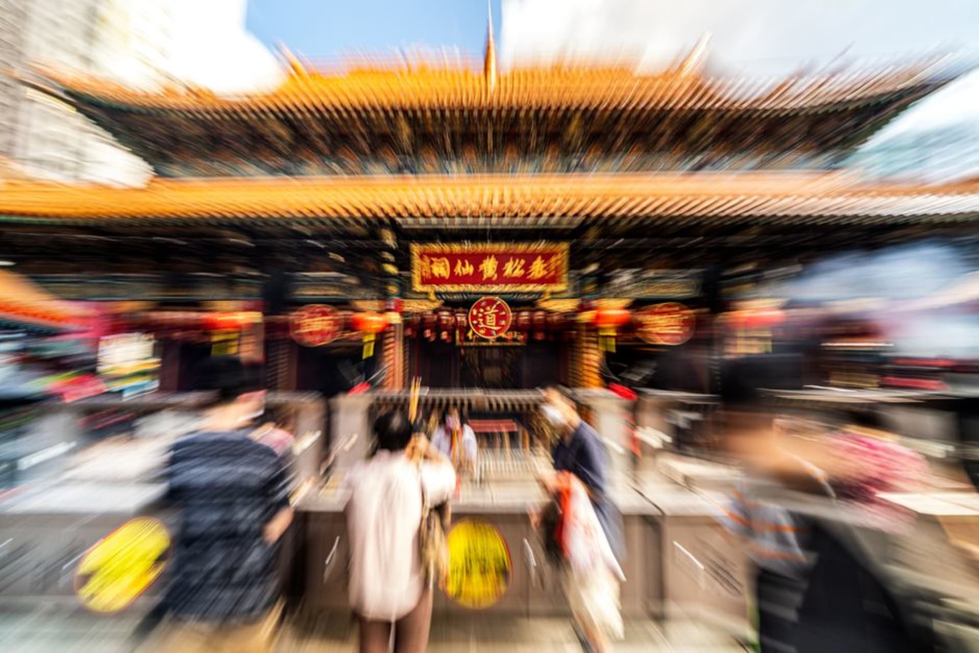 Devotees burning incense in front of the ornate red and gold main hall at Wong Tai Sin Temple