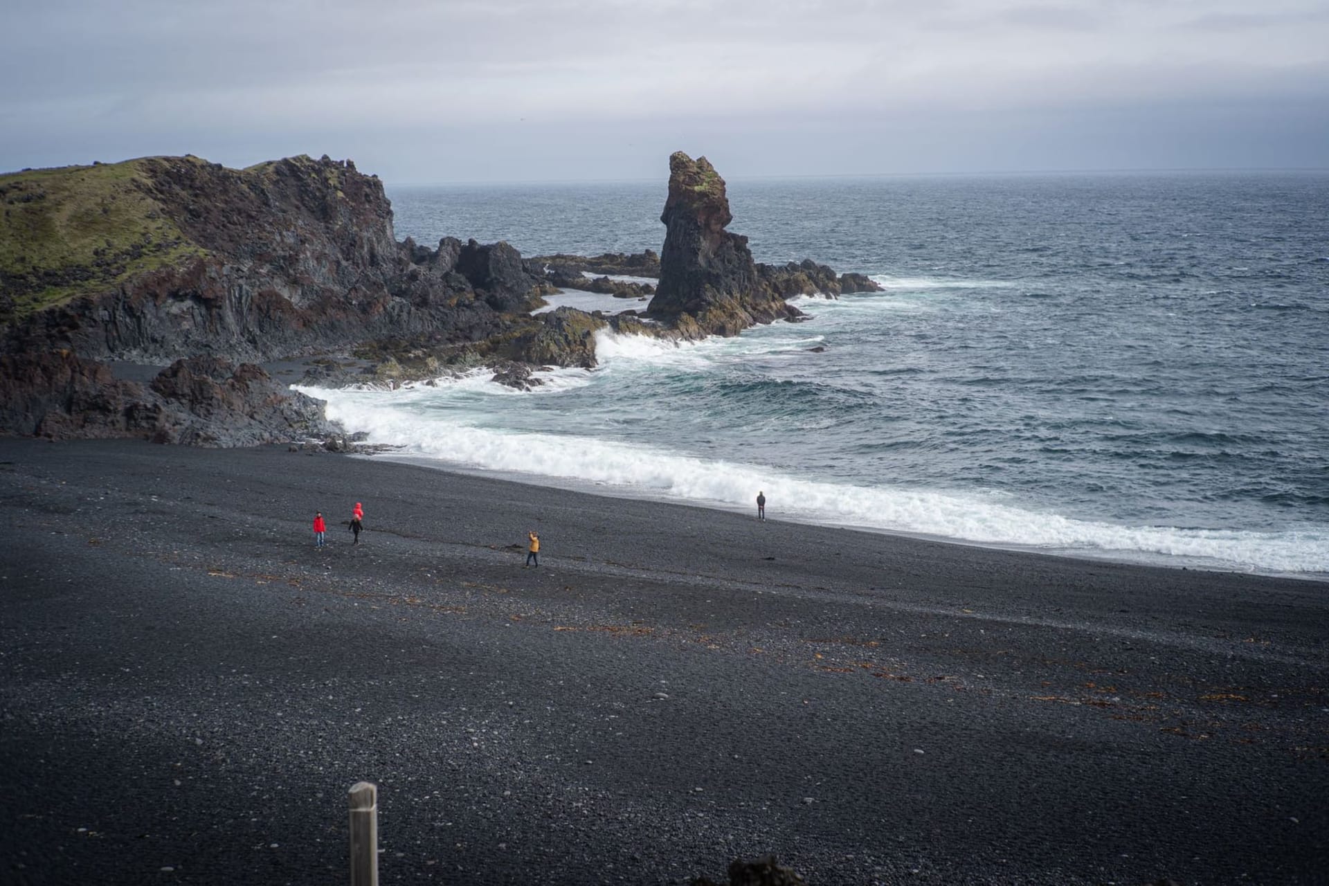 A vast expanse of dark jagged lava field stretching toward a sulfurous steam plume rising against a pale arctic sky on Iceland's Reykjanes Peninsula