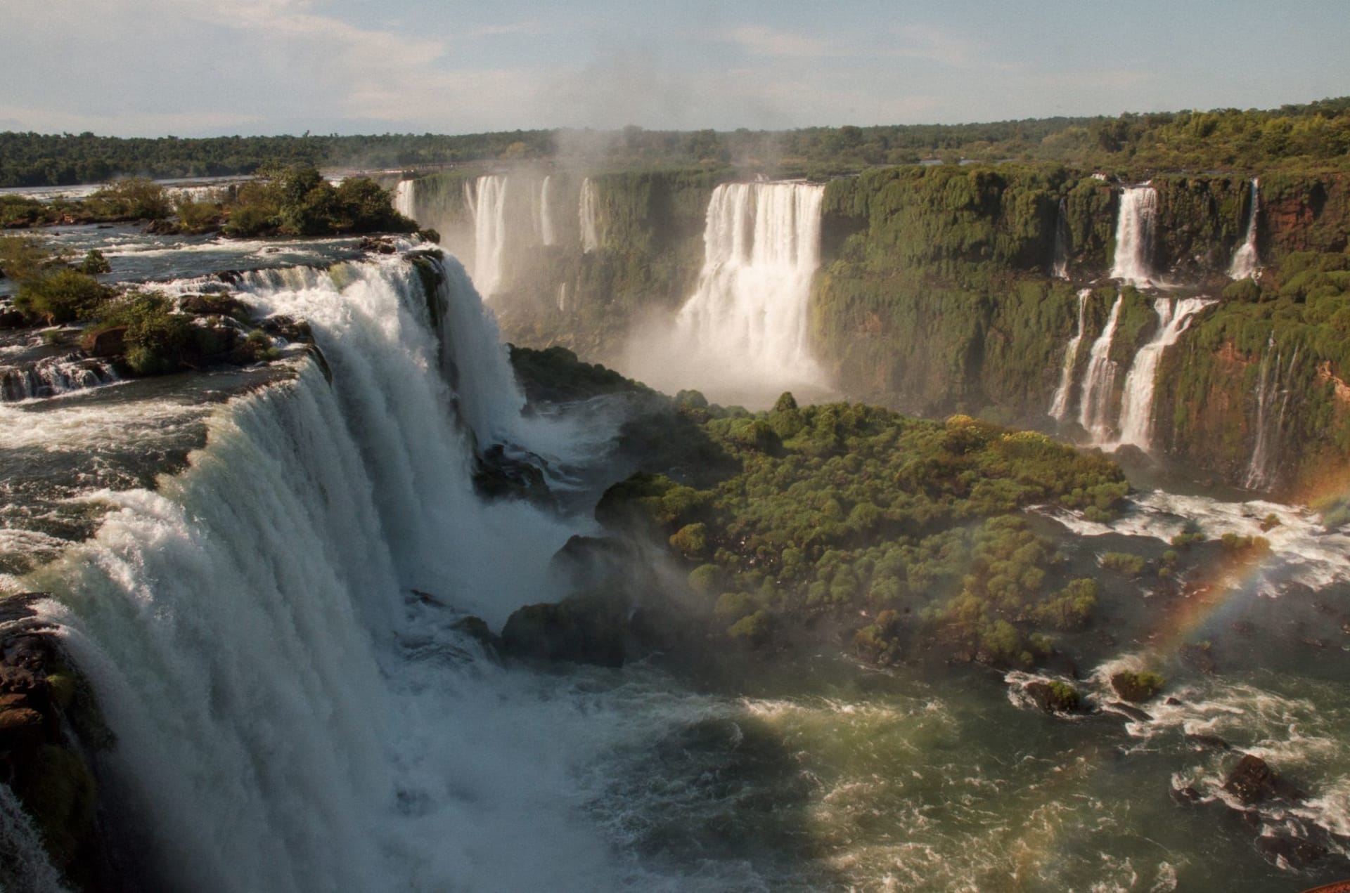Iguazú Falls cascading over lush rainforest with mist rising and a rainbow arching above the water