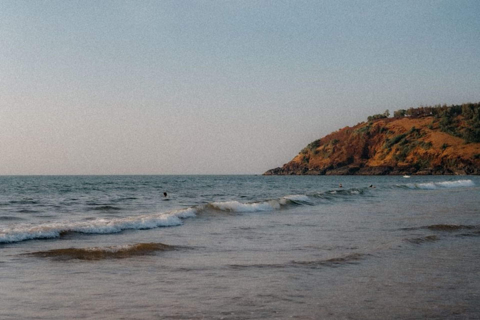 Golden sand crescent of Om Beach curling between two forested headlands at sunset