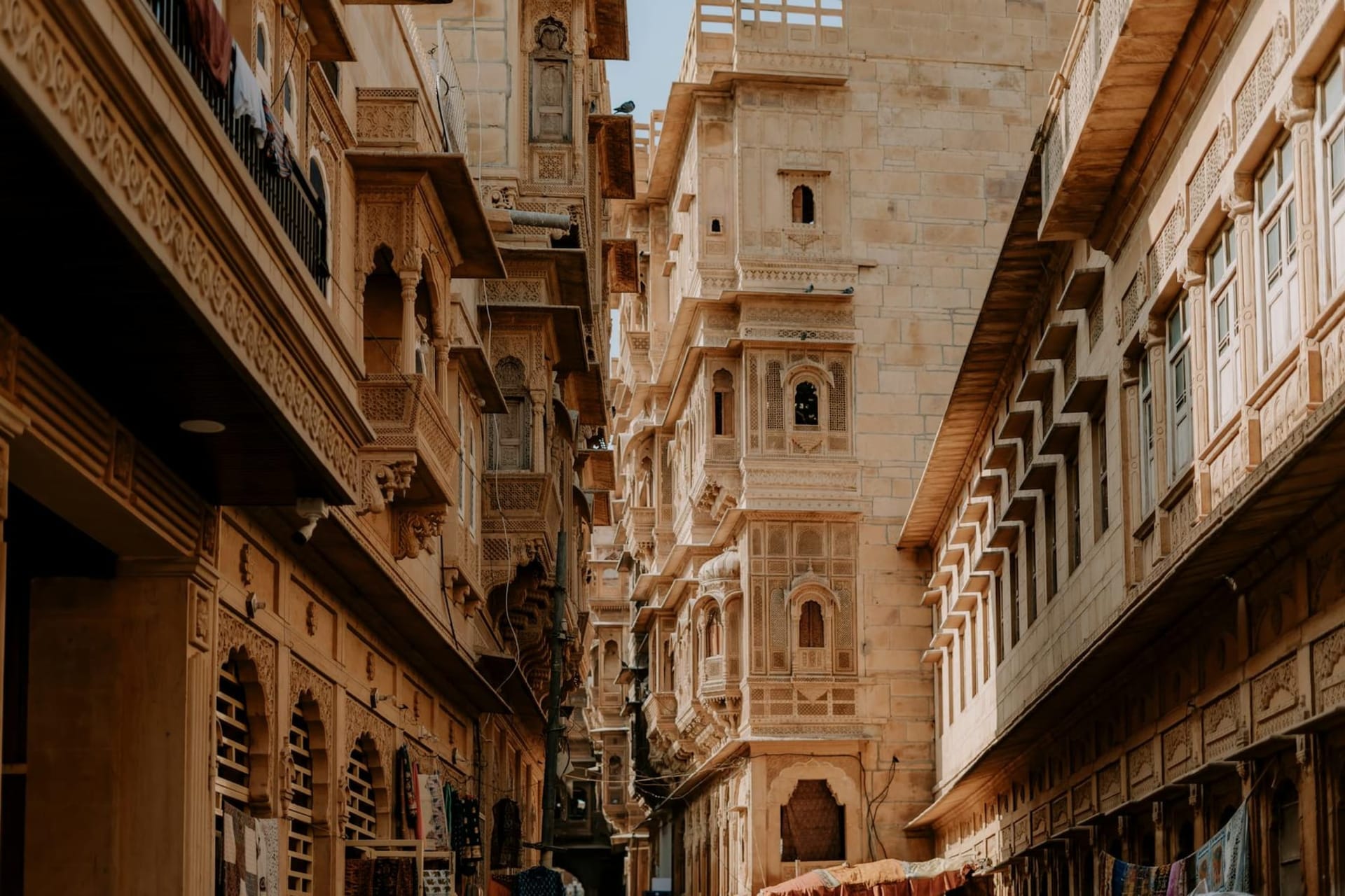 The golden sandstone towers of Jaisalmer Fort rising against a hazy desert sky at dusk, warm amber light catching every carved facade and battlement