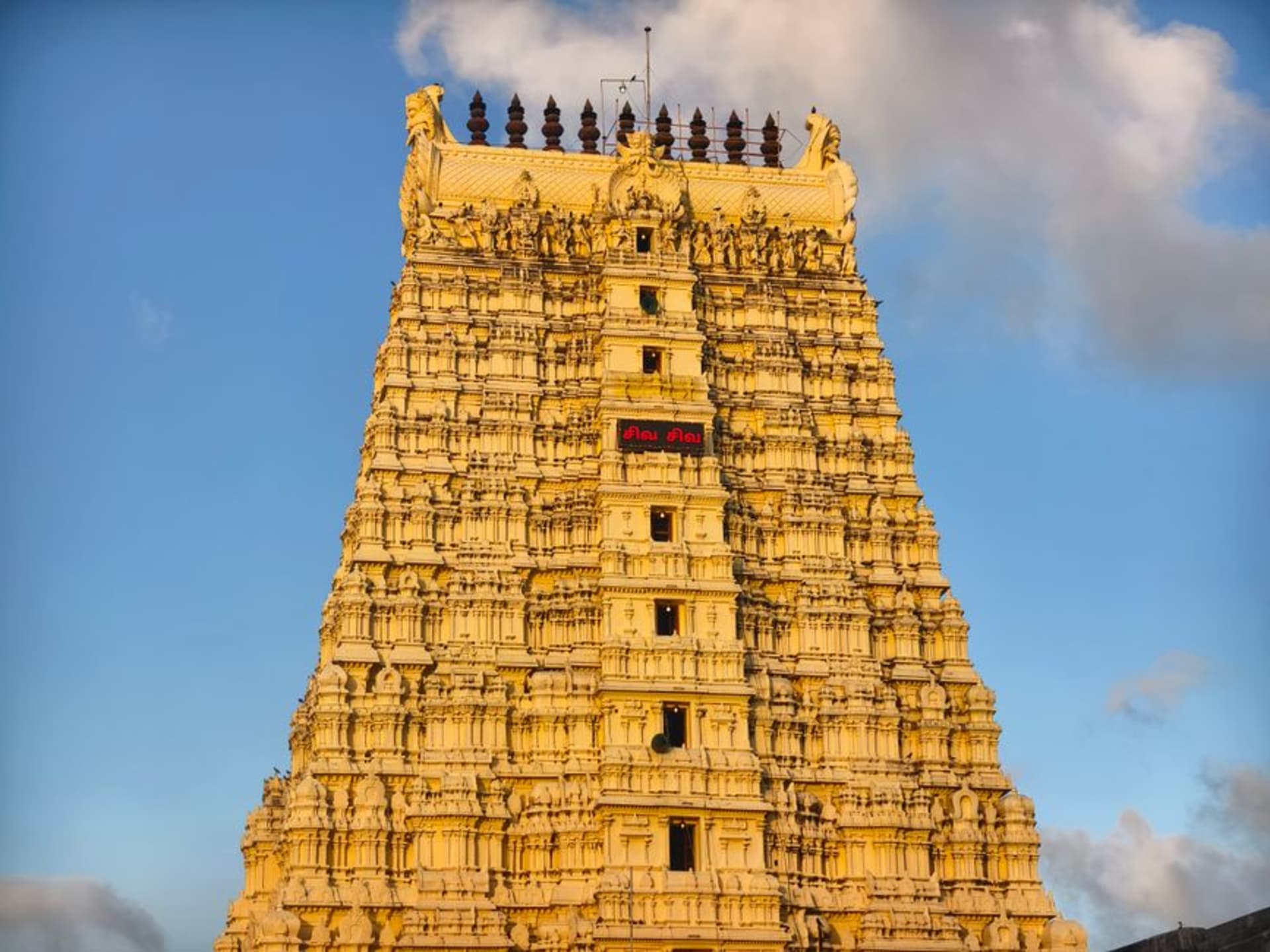 Krishna Matha temple gopuram illuminated at dusk with pilgrims gathered outside in Udupi