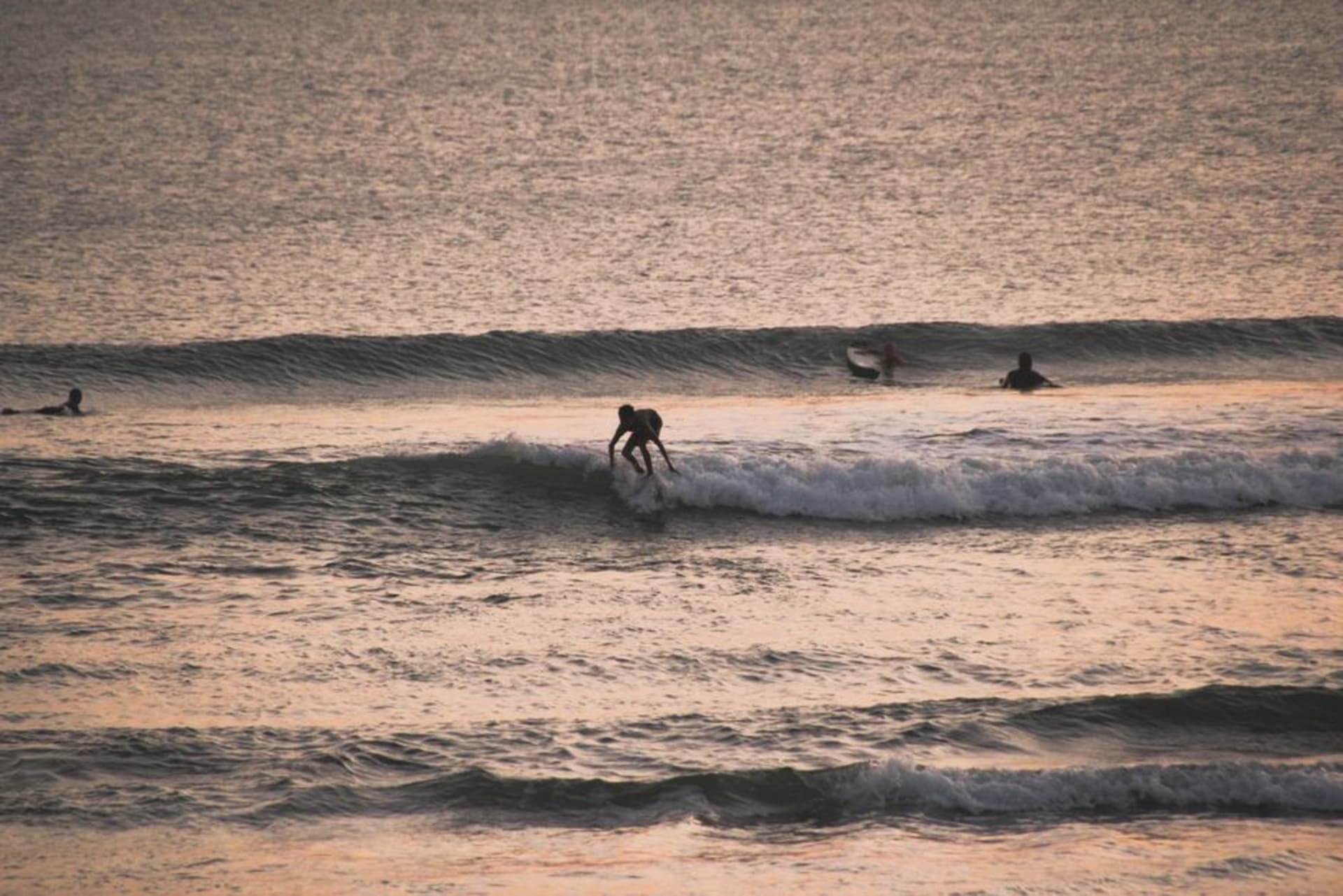 Black-sand beach at Canggu with surfers and a golden sunset over the Indian Ocean