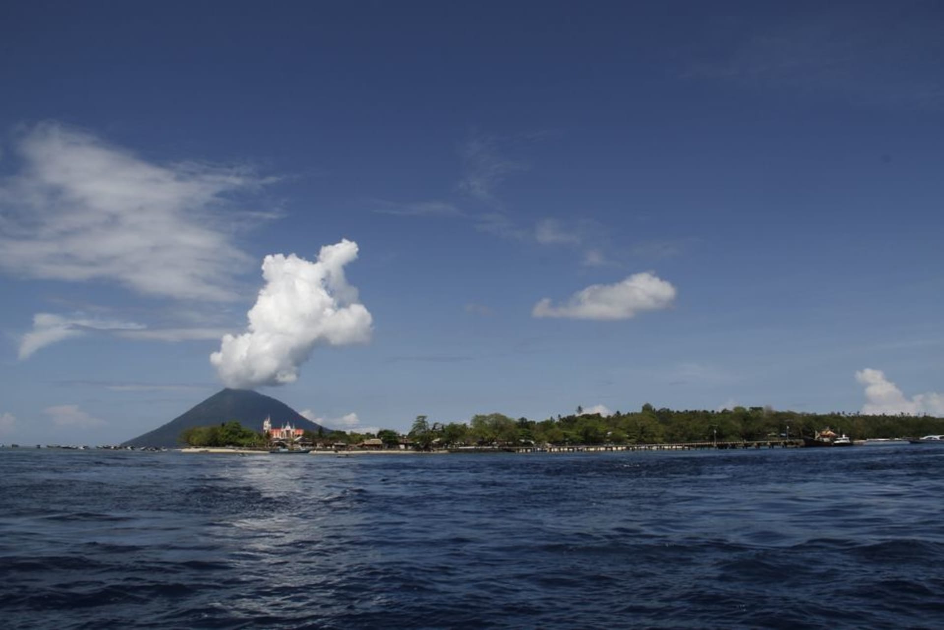 Manado's waterfront skyline at dusk with Mount Klabat in the background
