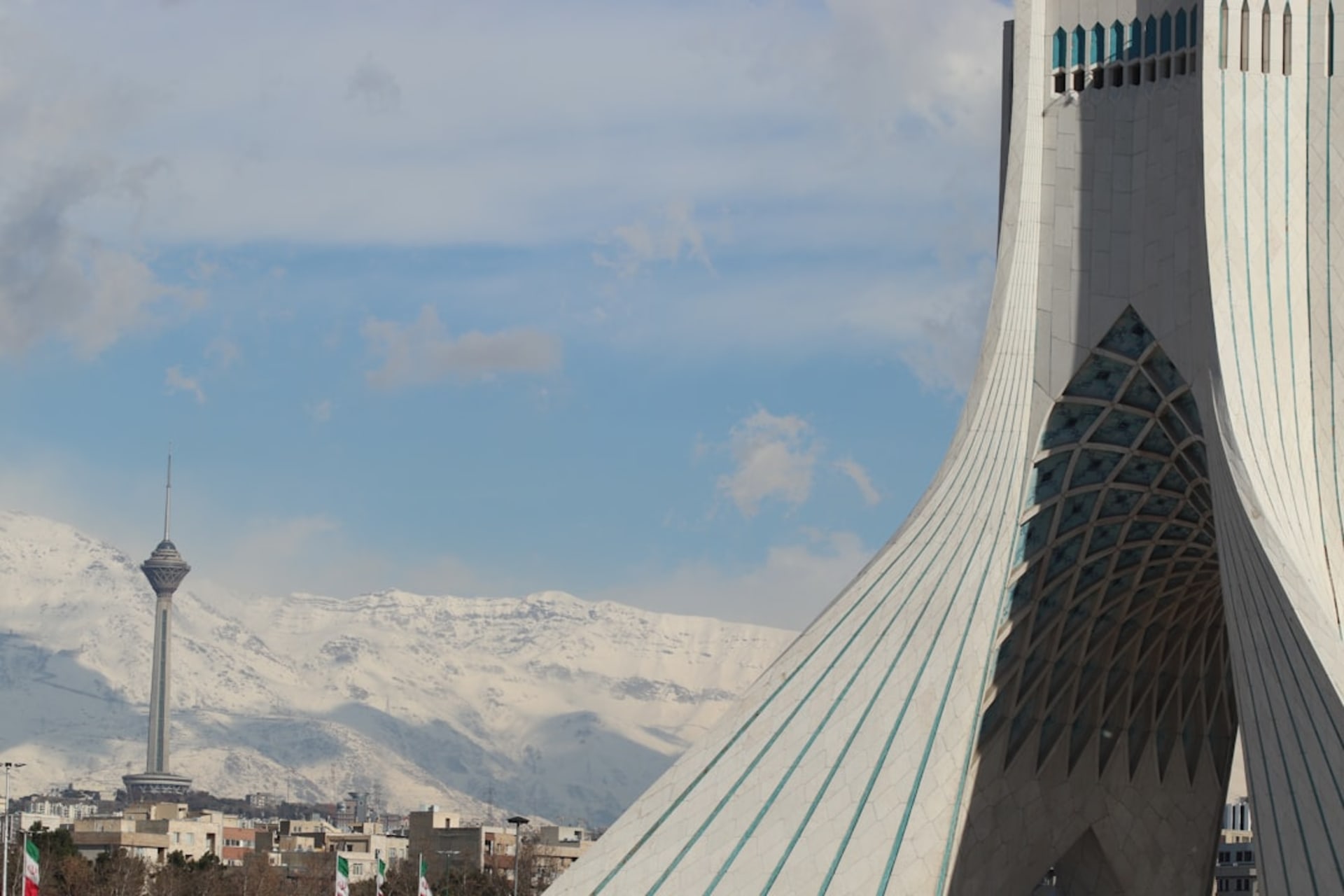 Milad Tower rising above the Tehran skyline at dusk, its lattice spire lit against a darkening sky with the Alborz mountains faint in the background