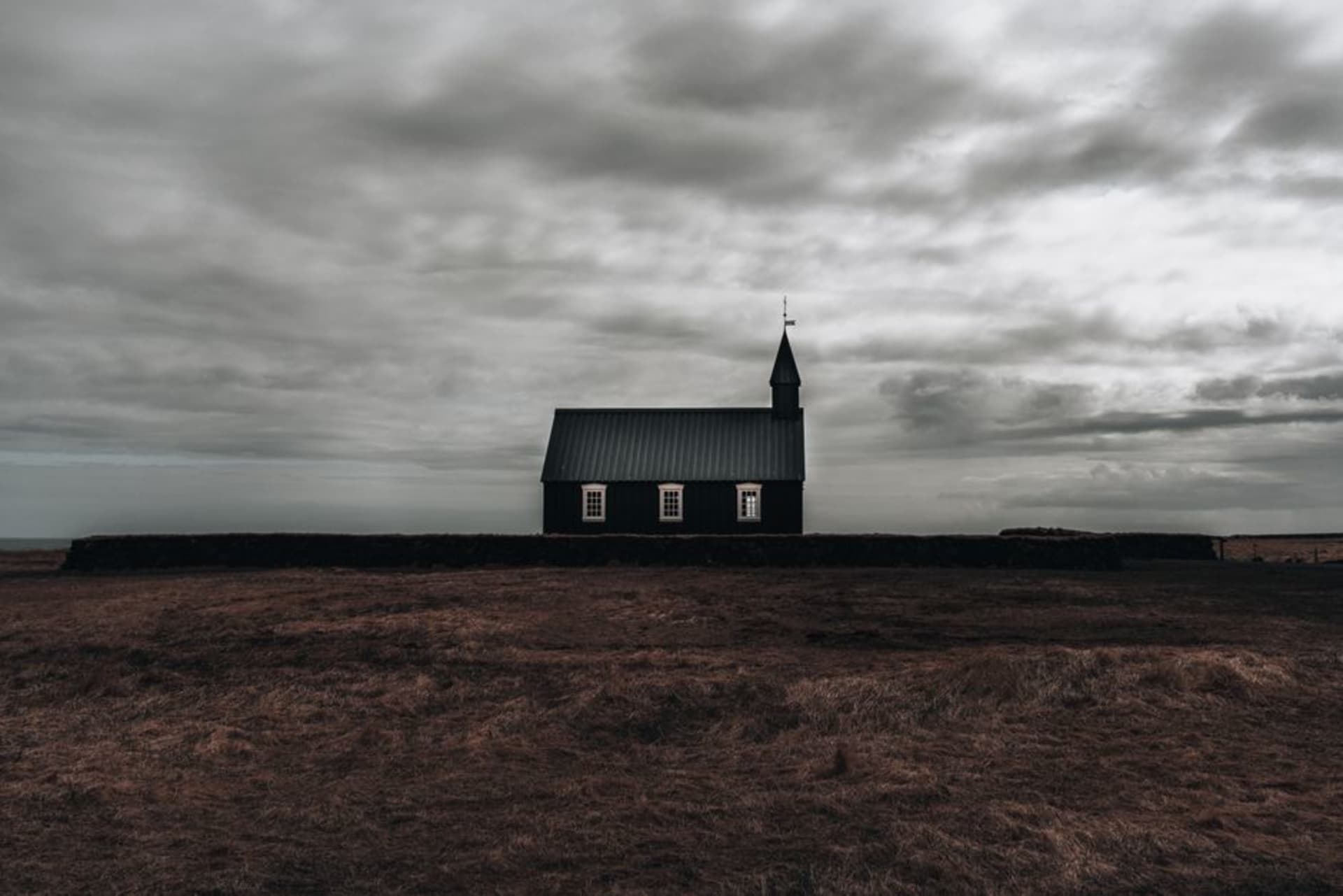 The dark volcanic stone exterior of Qareh Kelisa, the Black Church, set against green highland pasture near the Turkey border