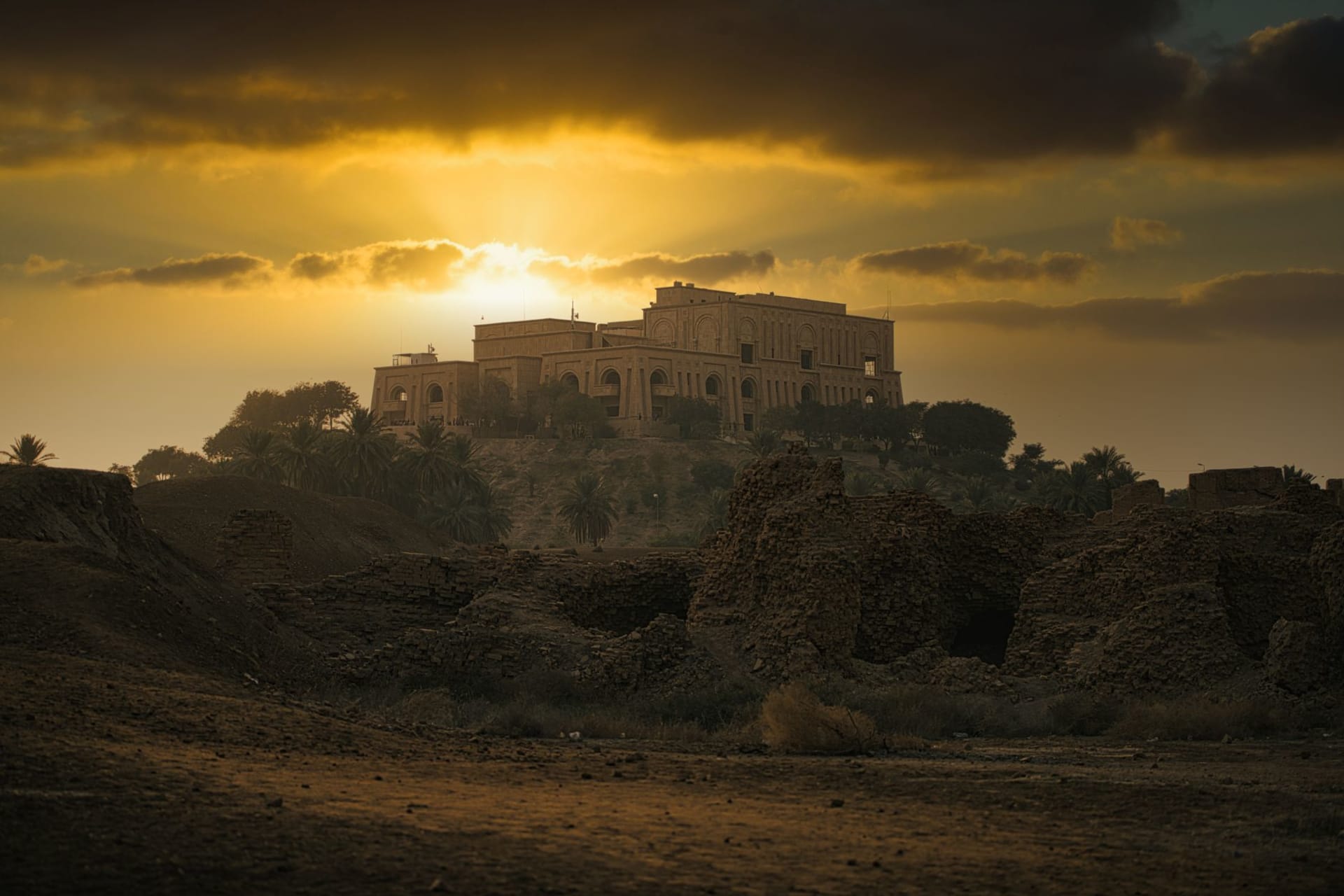 Dramatic sunset over Saddam Hussein's Palace in Babylon, the ruins silhouetted against a moody amber sky