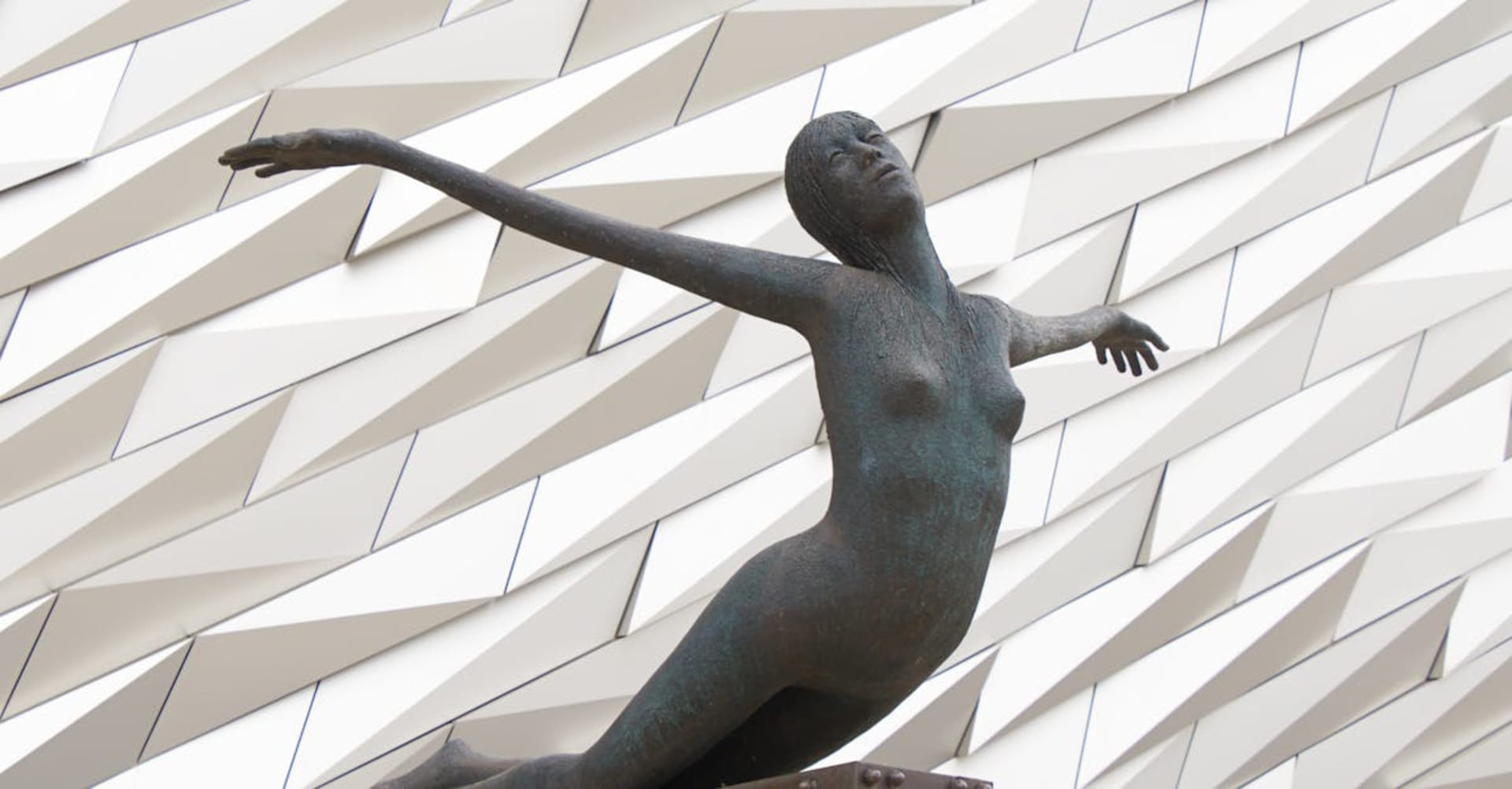 The Titanic Belfast museum with its angular aluminum facade reflected in the water of the old shipyard