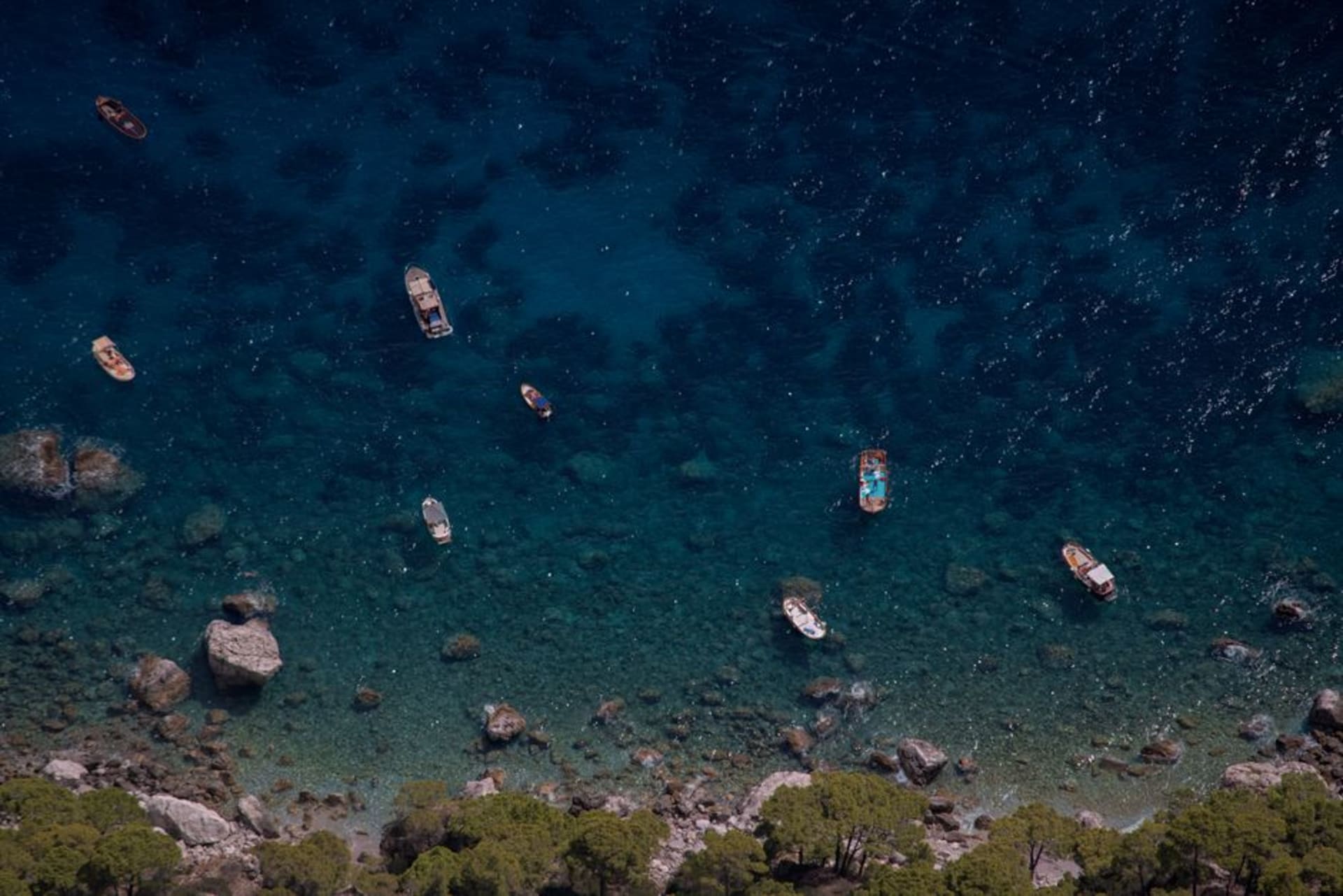 The limestone cliffs and turquoise water of Capri's coastline seen from a boat near the Faraglioni rock stacks