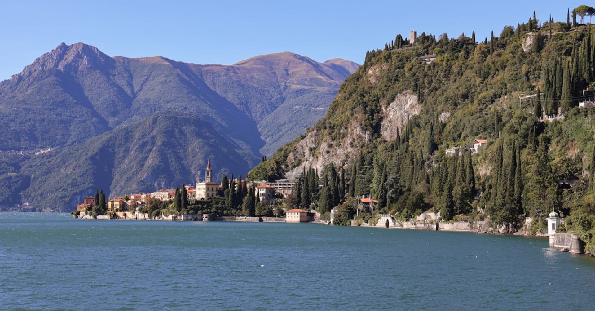A lakeside villa surrounded by cypress trees on the shores of Lake Como with mountains behind