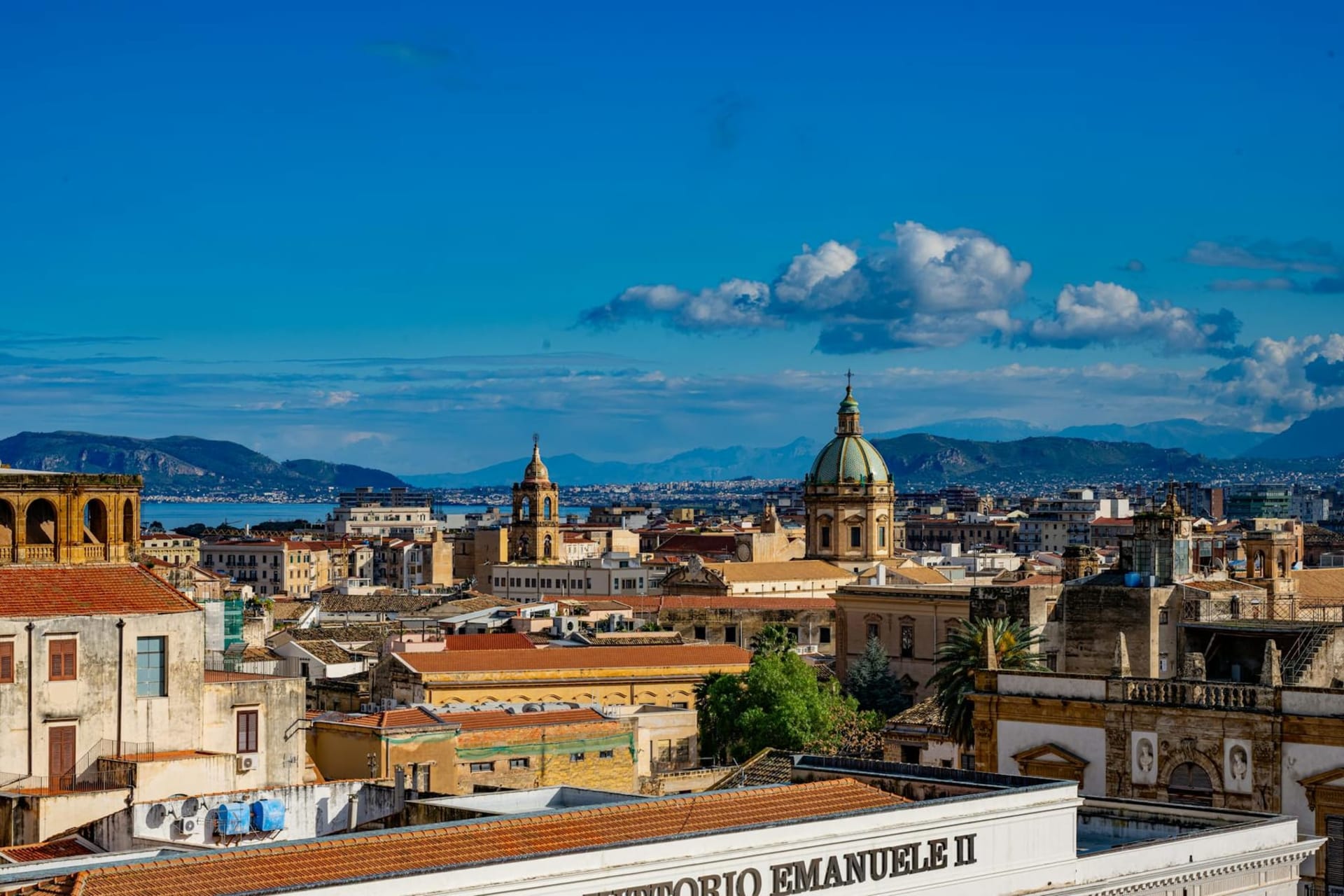 A sun-drenched Palermo street market with vendors selling spices, produce, and fresh fish beneath baroque church facades and tangled telephone wires