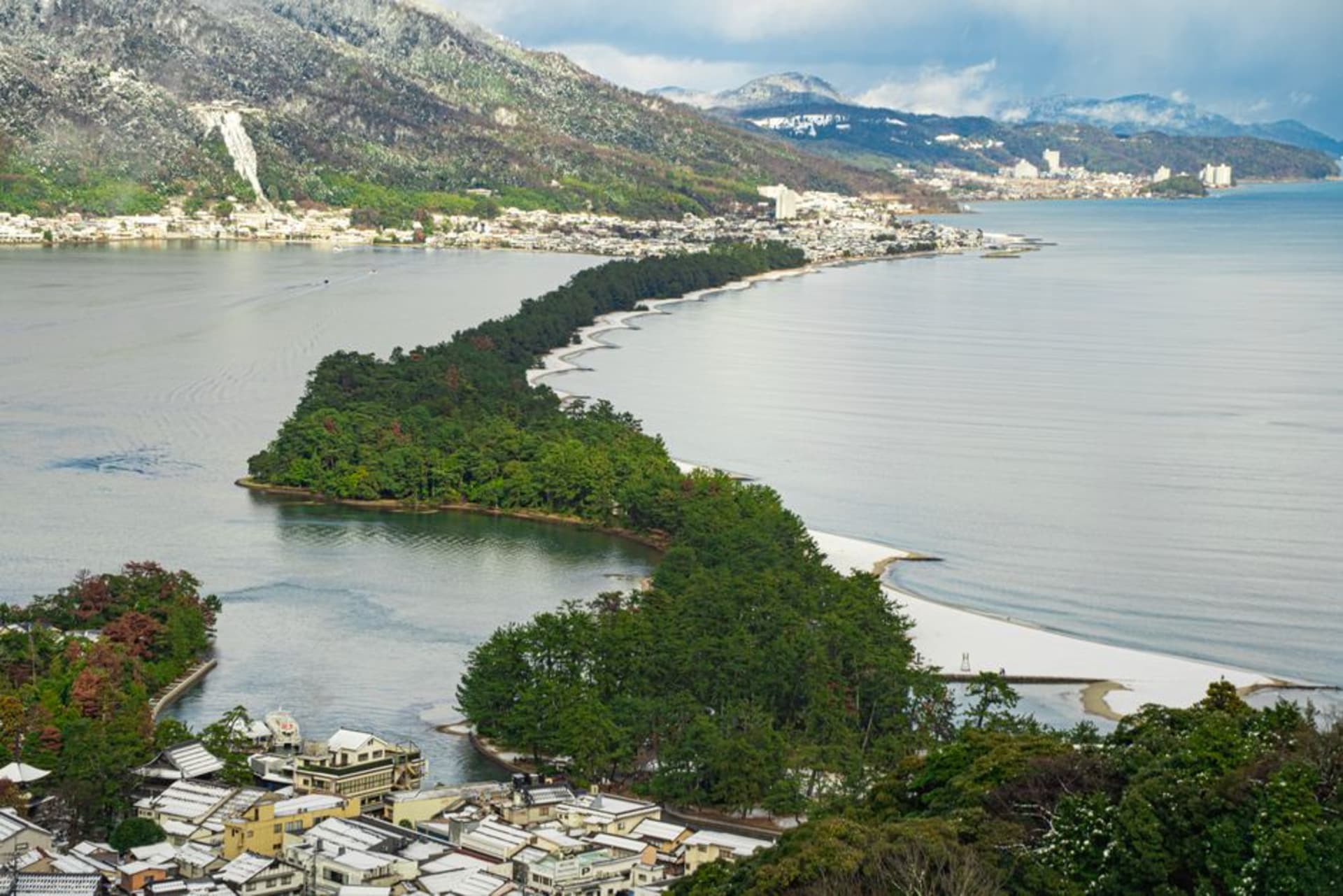 The pine-covered sandbar of Amanohashidate stretching across the blue bay, seen from the hillside viewpoint above