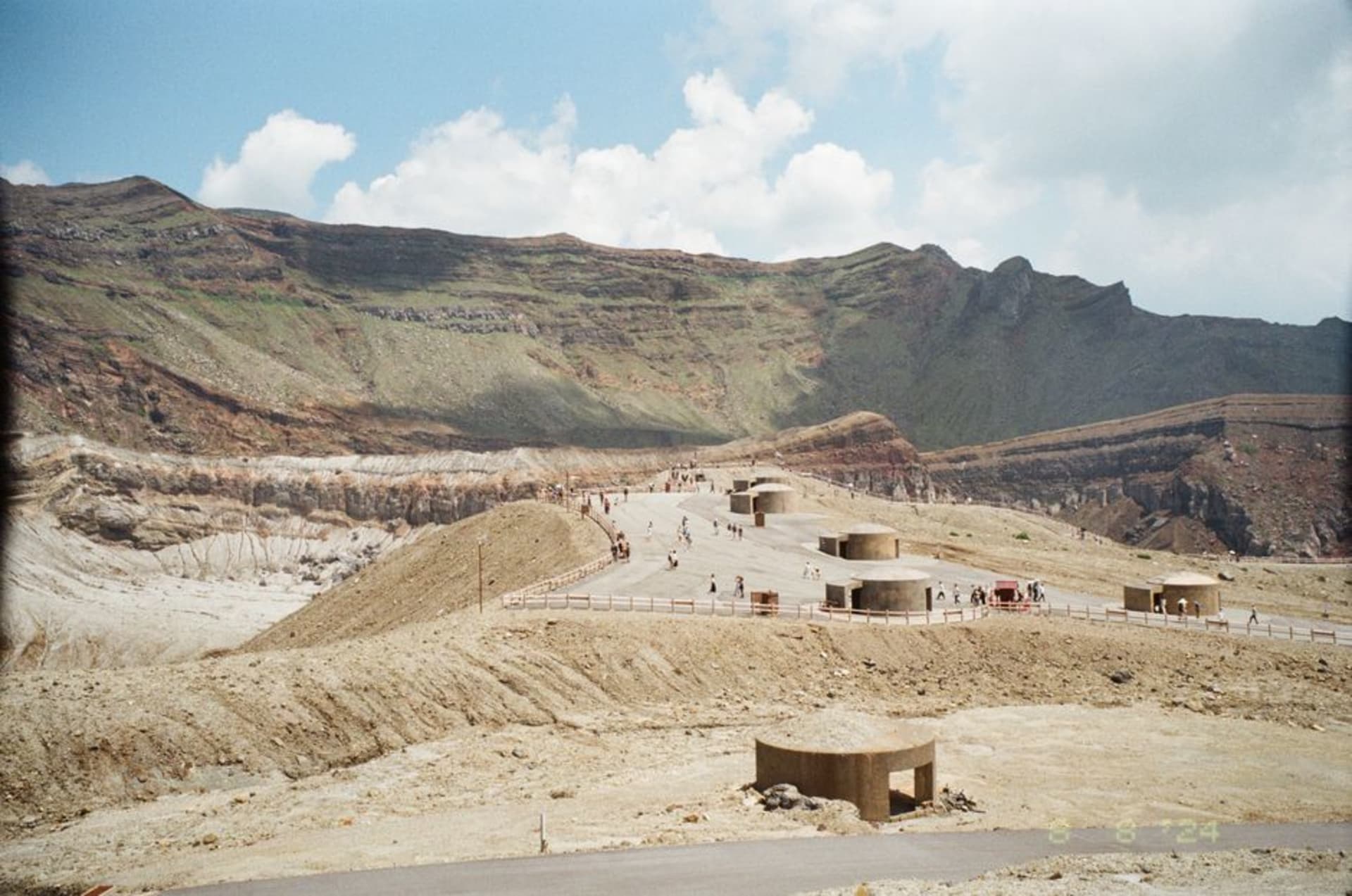 The wide green grasslands of the Aso caldera under a big sky, ringed by distant volcanic ridges