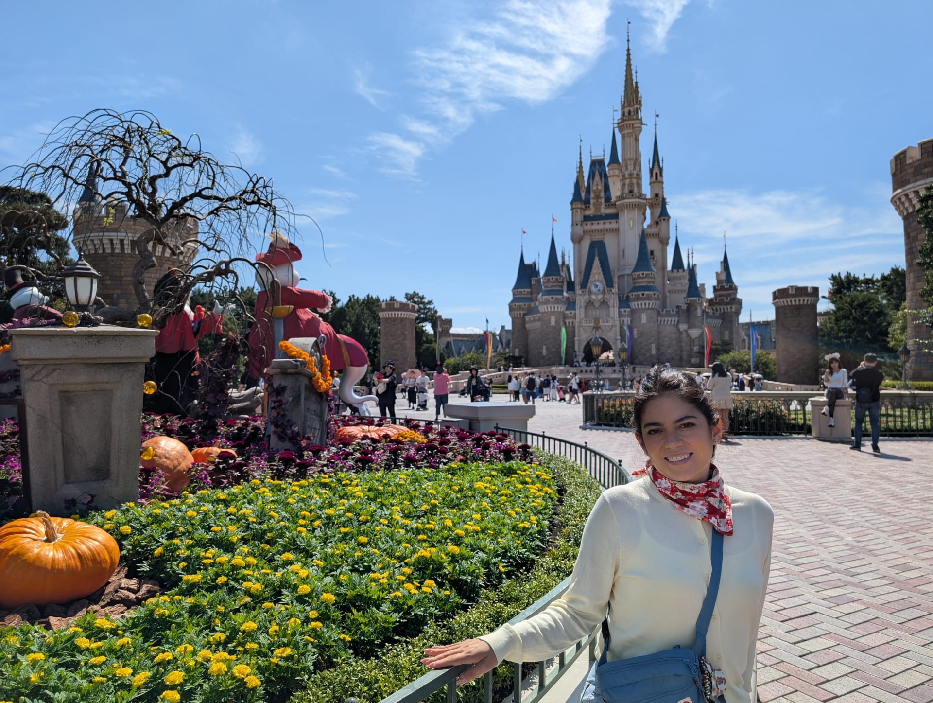 Lia in front of Cinderella Castle at Tokyo Disneyland with Halloween pumpkins and autumn flowers