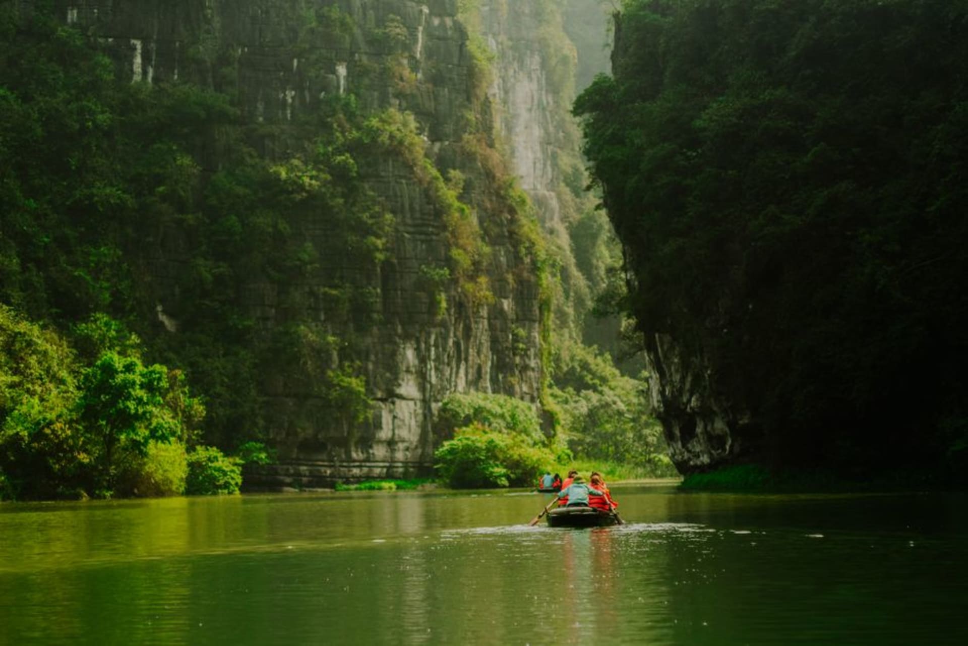 Poled wooden boat drifting beneath towering limestone cliffs on the Satetsu River at Geibikei Gorge