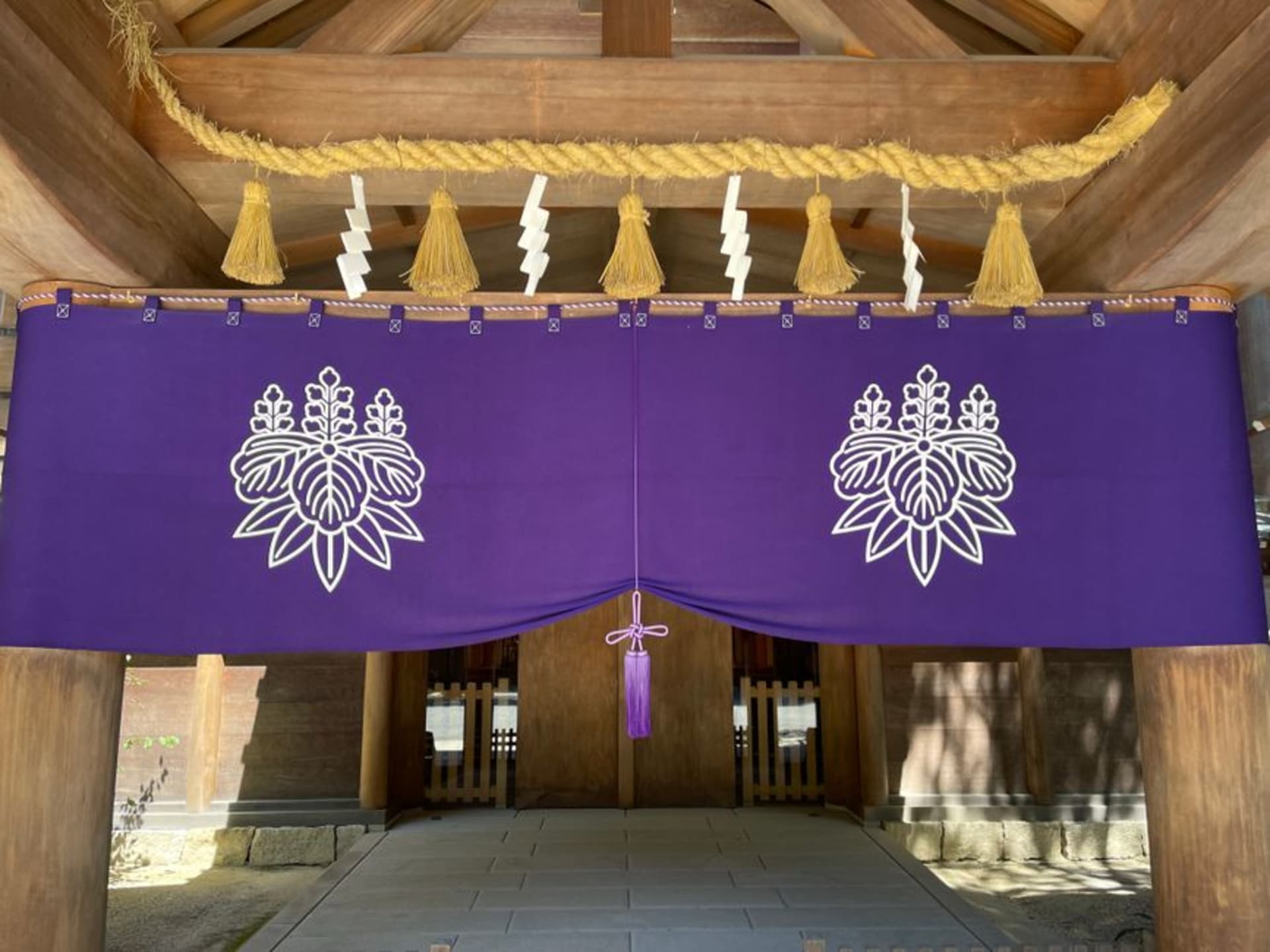 The great shimenawa straw rope hanging beneath the eaves of a hall at Izumo Taisha, thick as a tree trunk and twisted, worshippers small beneath it