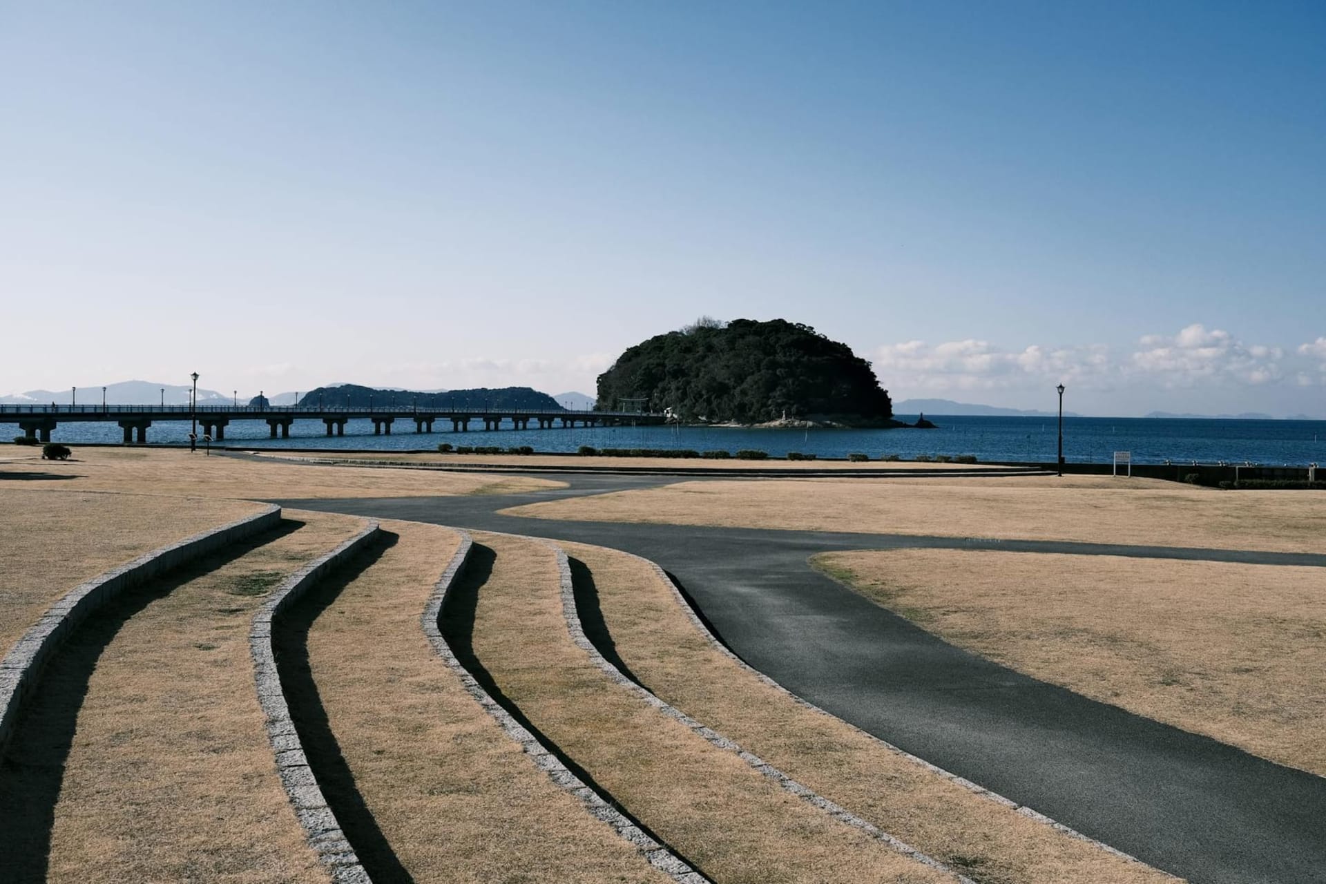 Terraced rice paddies cascading toward a calm grey-blue sea on Teshima island, with a wooden fishing boat moored at a small dock in the distance
