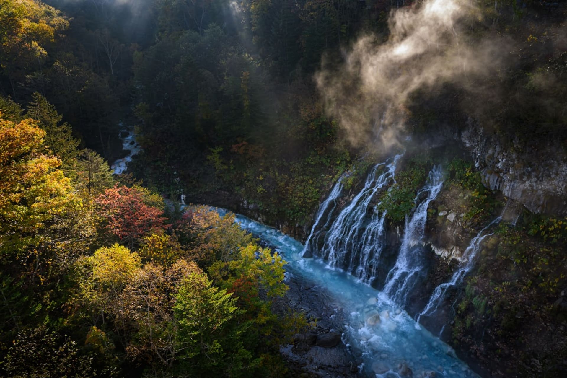 The forested Toyohira River gorge at Jōzankei ablaze with red and orange autumn foliage, a bridge crossing above the water