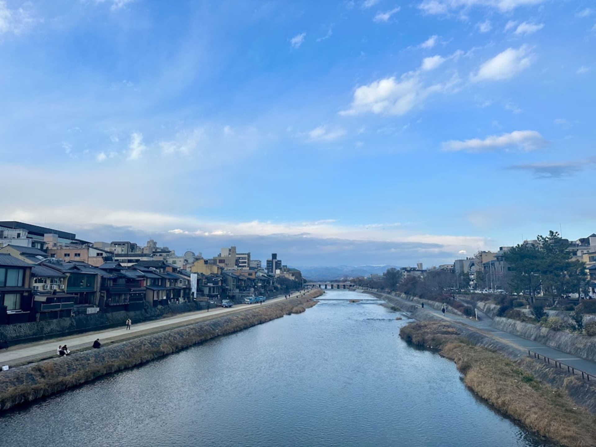 The Pacific coast at Kamogawa, a long grey-sand beach curving beneath low green hills with surfers small on the swell
