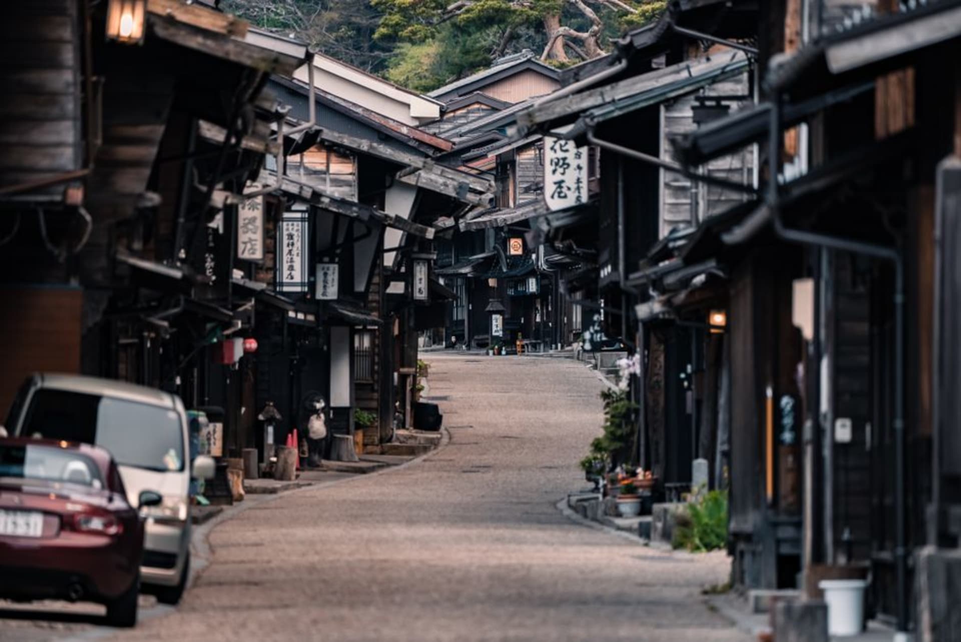 Wooden houses stacked steeply above the rushing Kiso river in Kiso-Fukushima, forested mountains rising behind under grey cloud