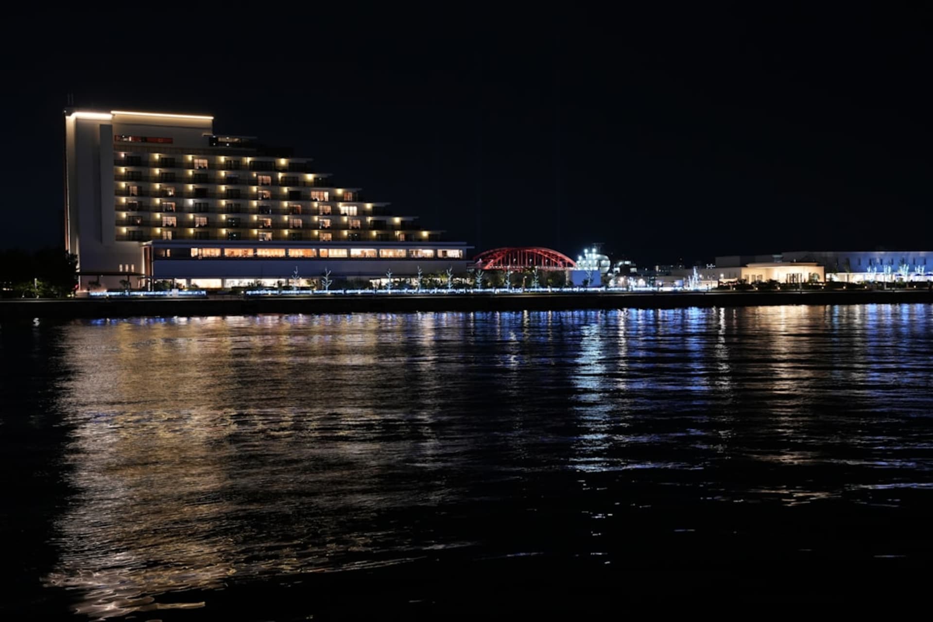 Kobe harbor at dusk with the red Port Tower and the wave-roofed Maritime Museum lit up against the water