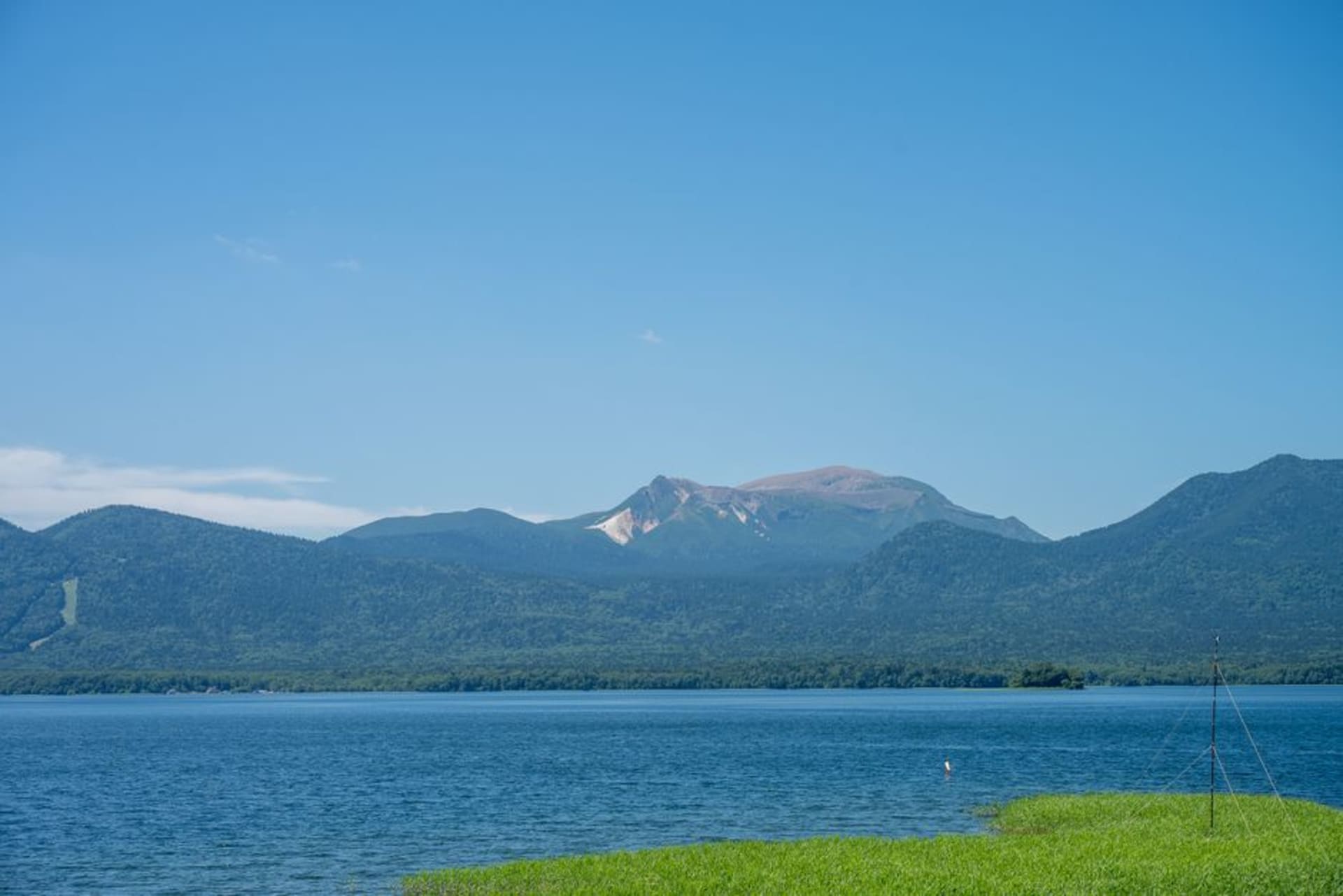 Lake Akan ringed by forested volcanic hills under a still morning sky, eastern Hokkaidō