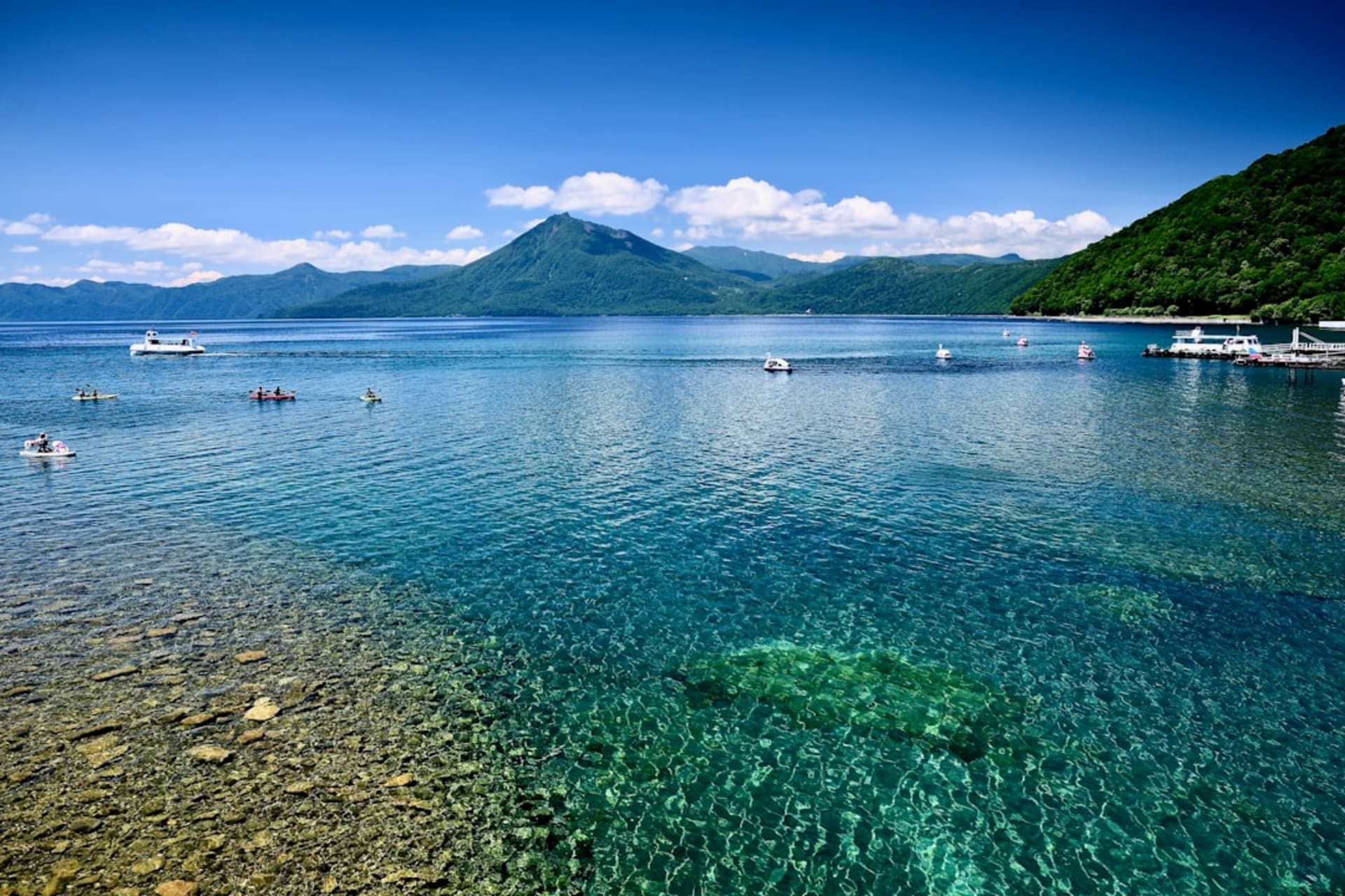 The circular caldera of Lake Toya with its wooded central island, ringed by green hills and volcanic peaks