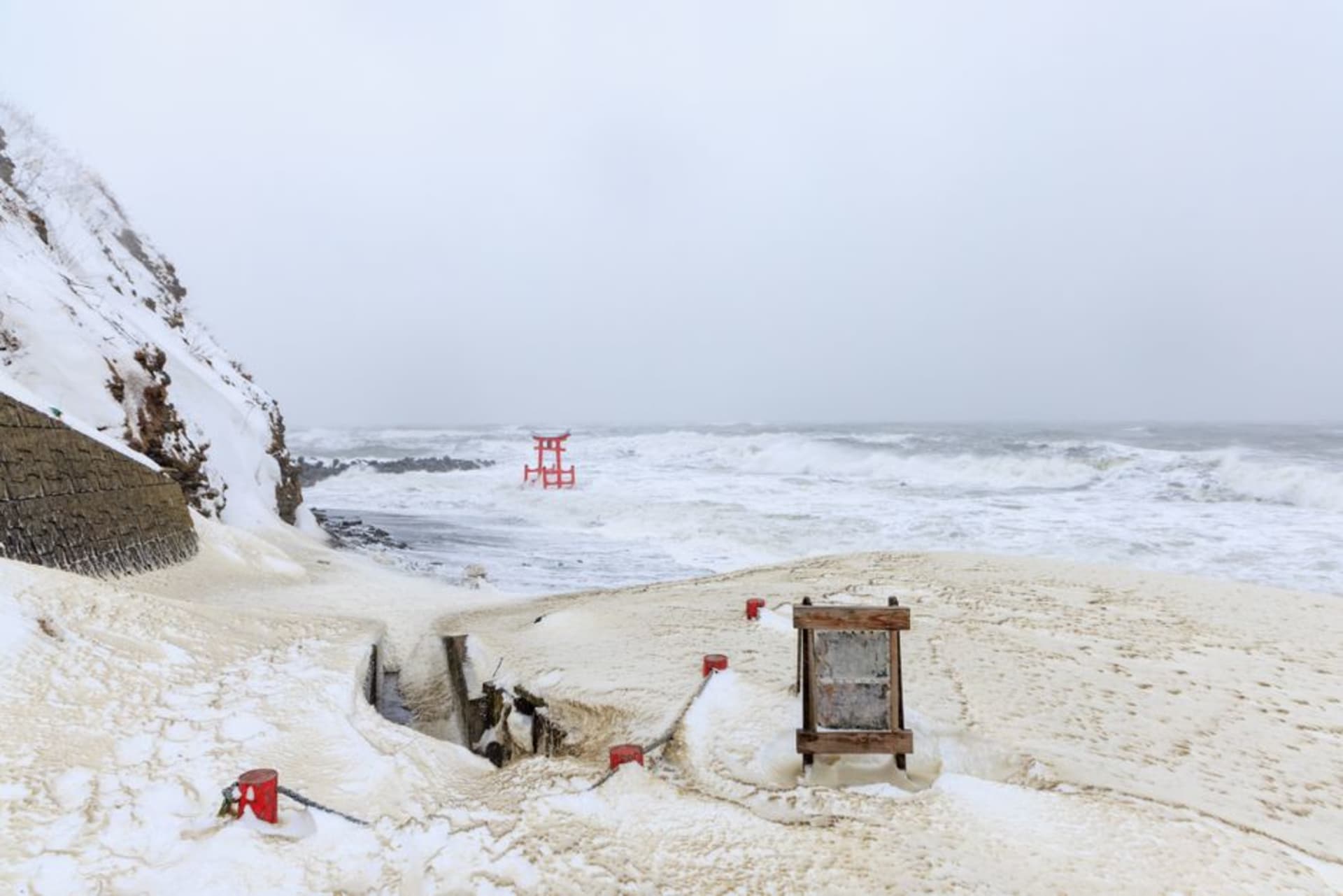 A cascade of 123 red torii gates descending a green cliff toward the sea at Motonosumi, Yamaguchi