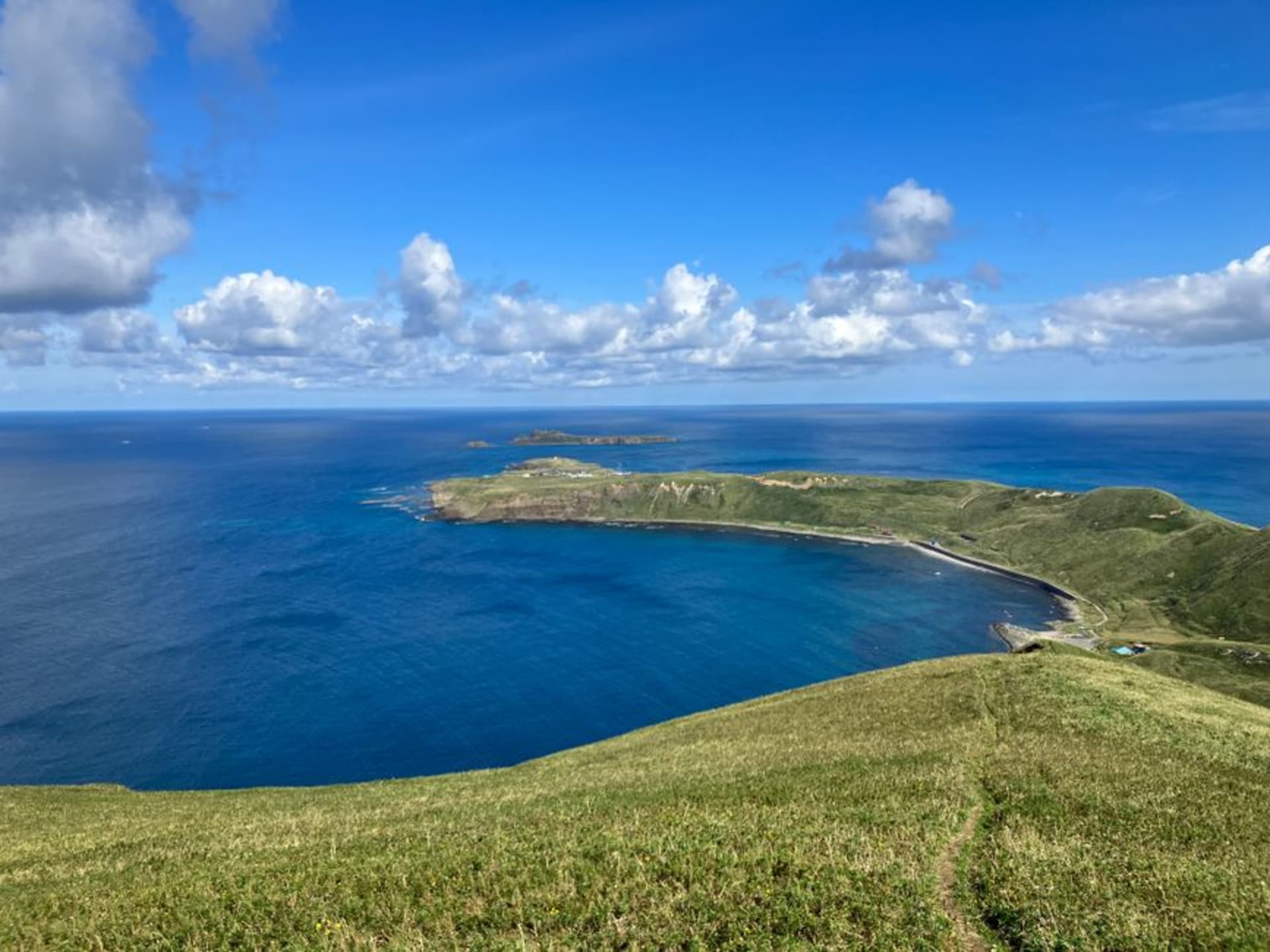 The green rolling meadows of Rebun Island meeting sea cliffs, wildflowers in the foreground and the ocean beyond