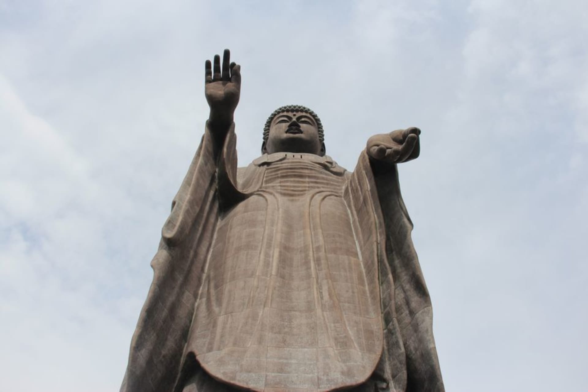 The colossal bronze Ushiku Daibutsu towering over flower gardens against a blue sky